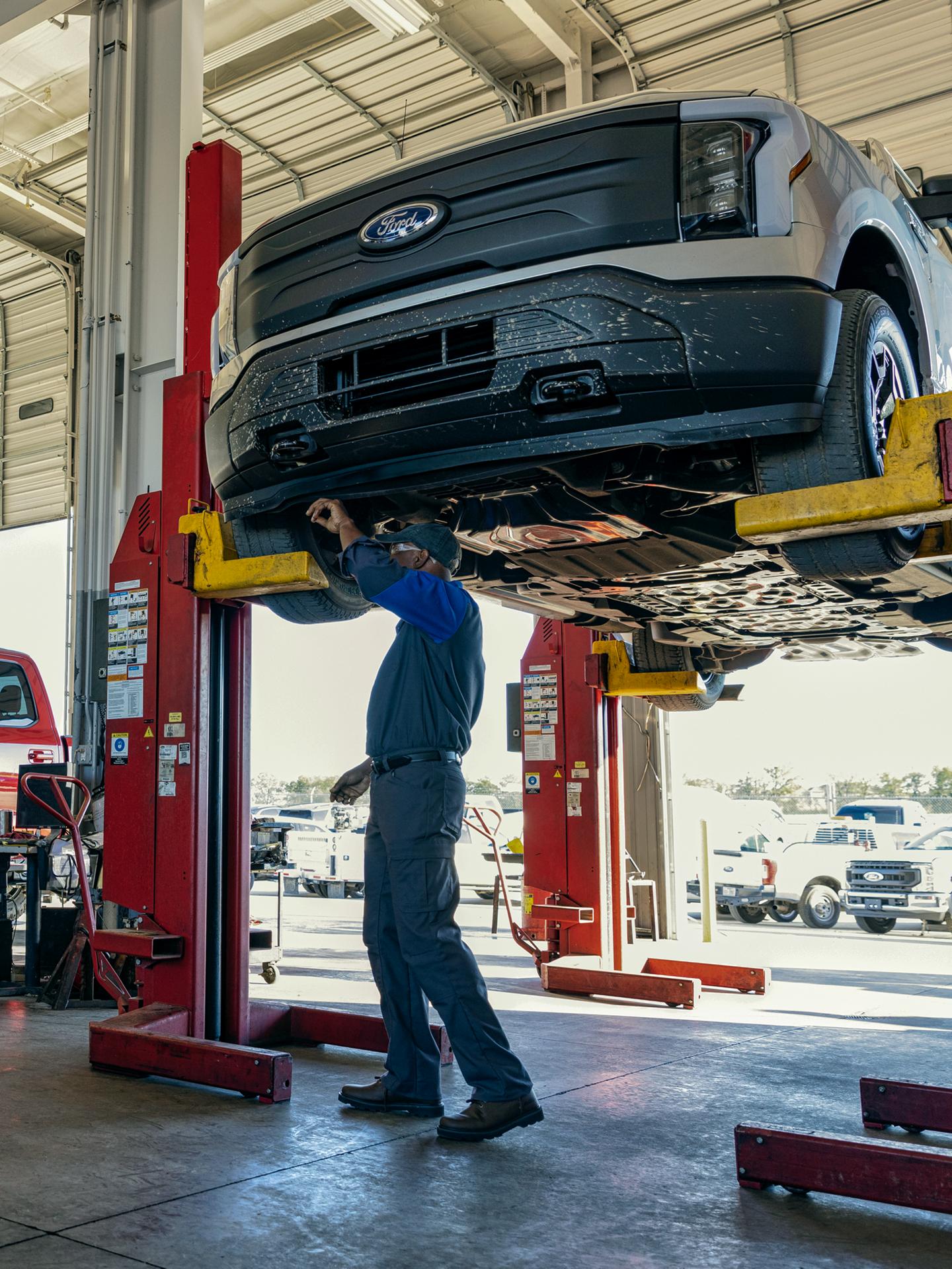 A Ford technician works on an F-150 Lighting on a lift in a service bay.