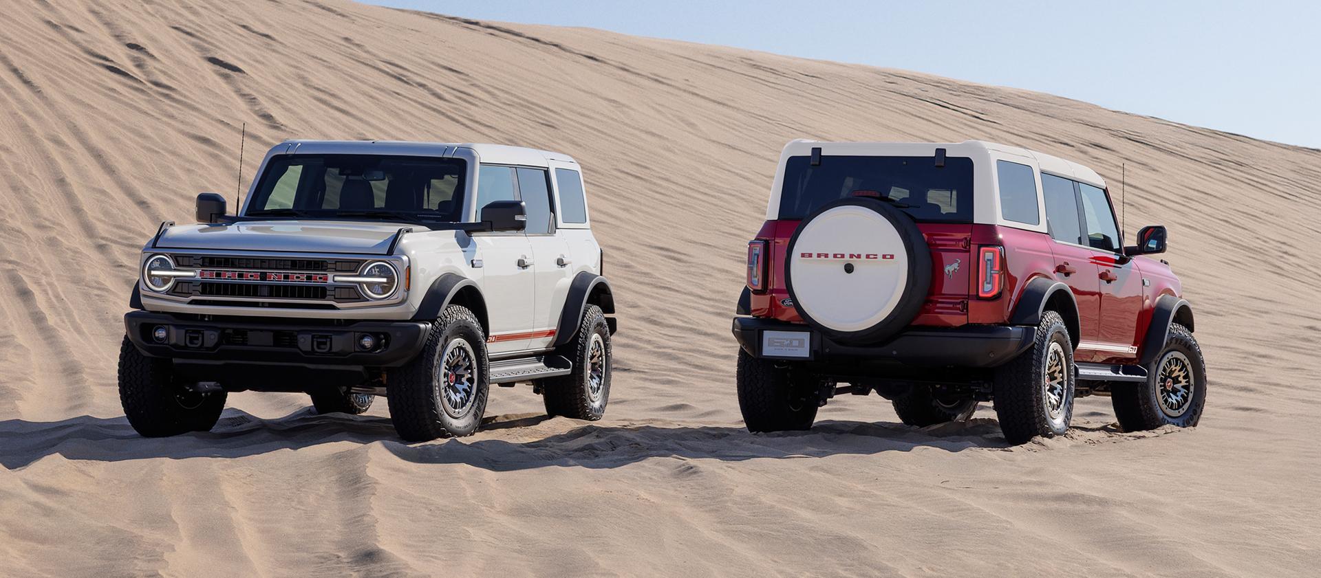 Two 2026 Ford Bronco® Outer Banks® SUVs with the available 60th Anniversary Package parked on a sandy expanse