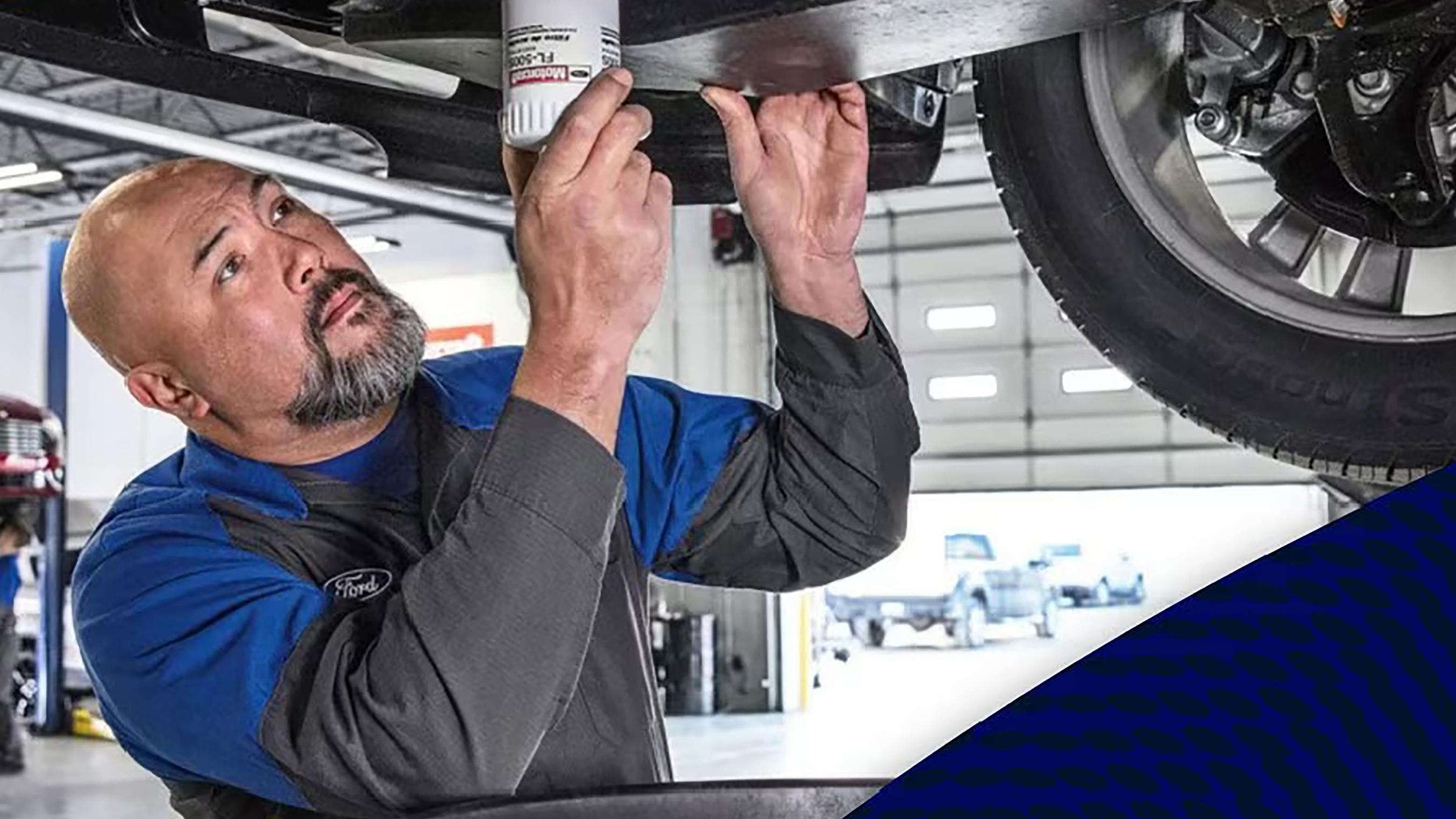 A Ford mechanic tightens the oil filter on a Ford vehicle hoisted up on the lift. 