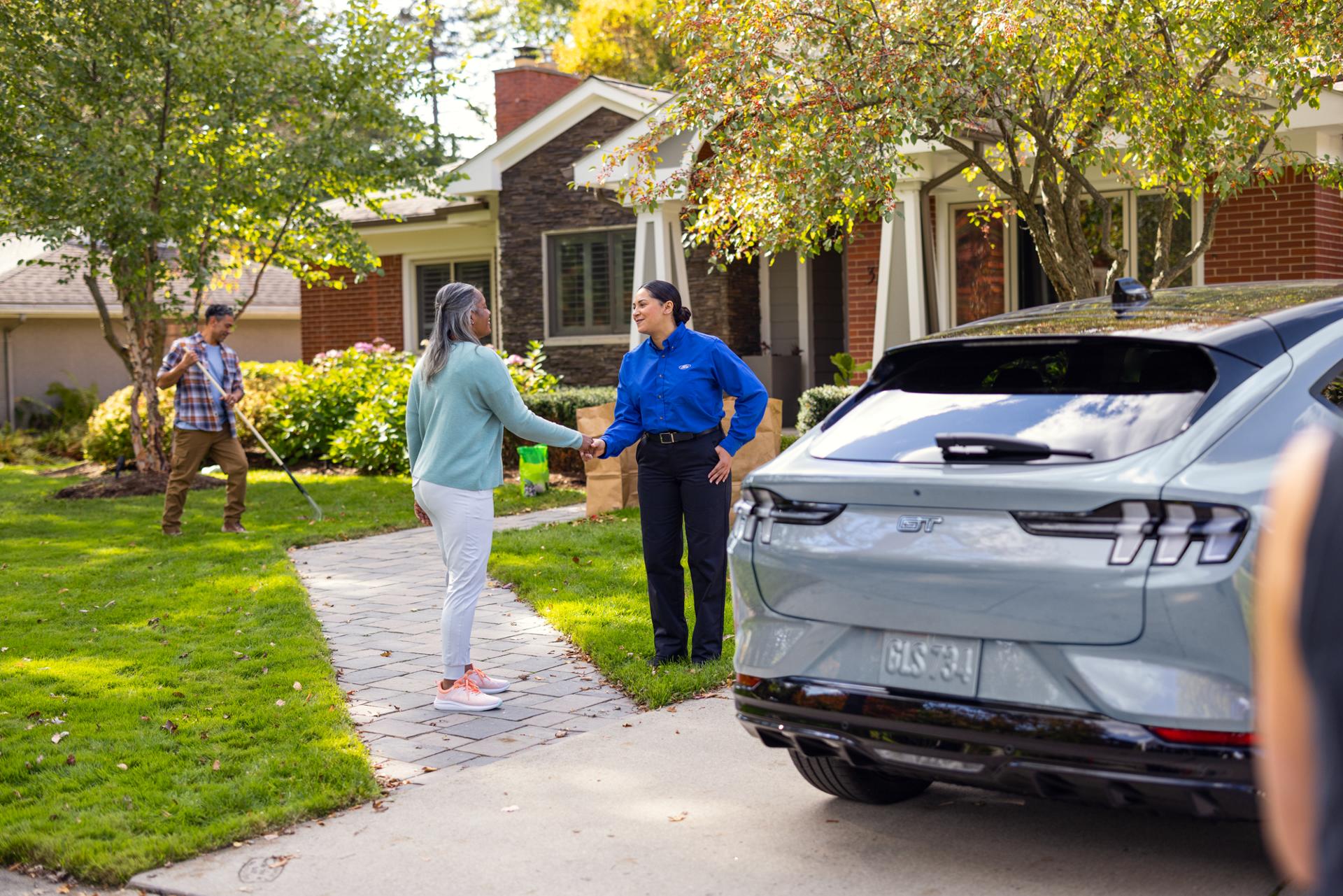Customer shaking hands with a Ford Service technician next to a Ford vehicle parked in a residential driveway.