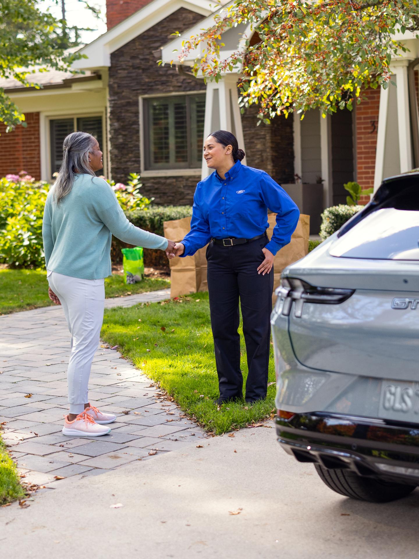 Customer shaking hands with a Ford Service technician next to a Ford vehicle parked in a residential driveway.