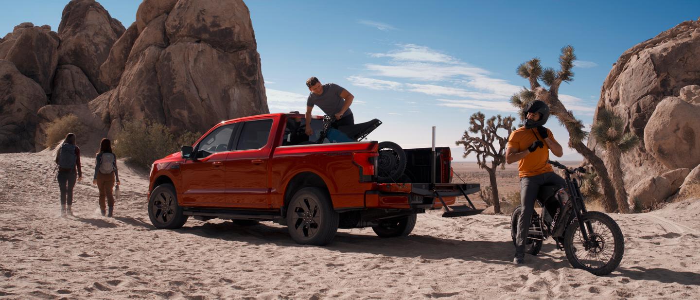 People near a 2025 Ford F-150® Lightning® pickup in the desert, with a dirtbike in the bed and one unloaded