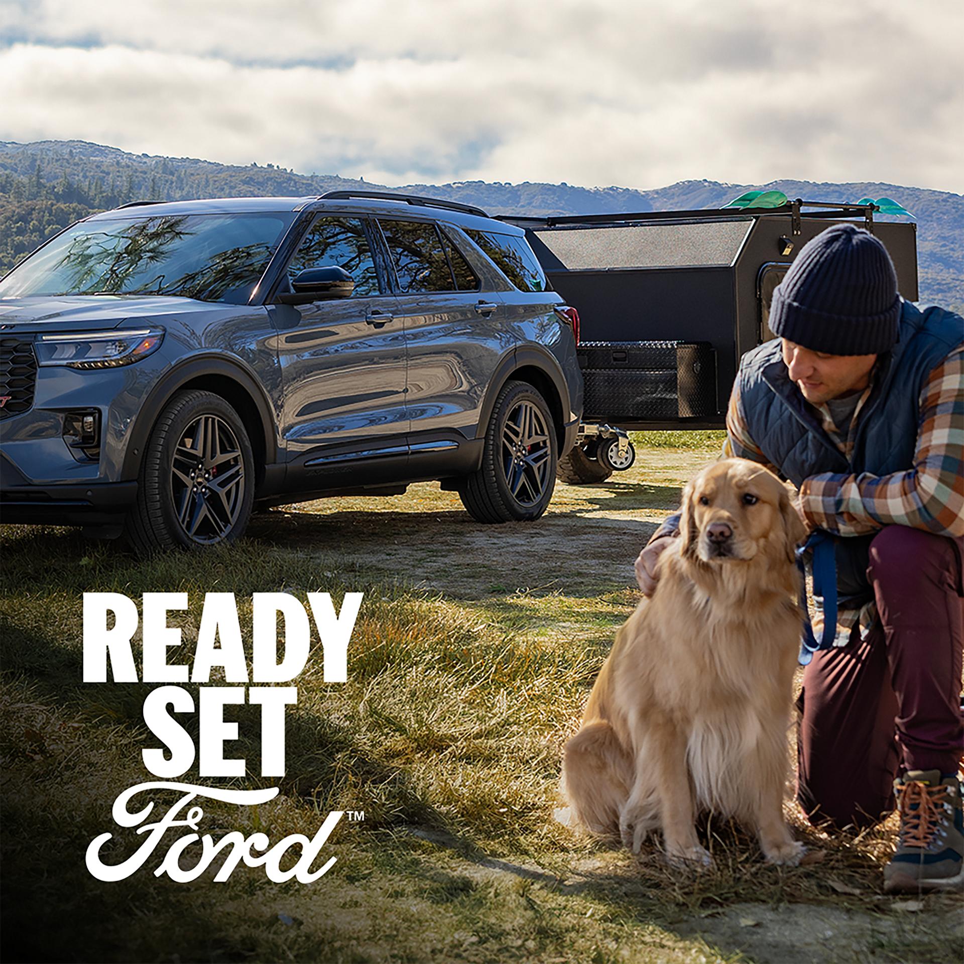 A 2026 Ford Explorer® parked outside towing a camper with a man and dog in the foreground