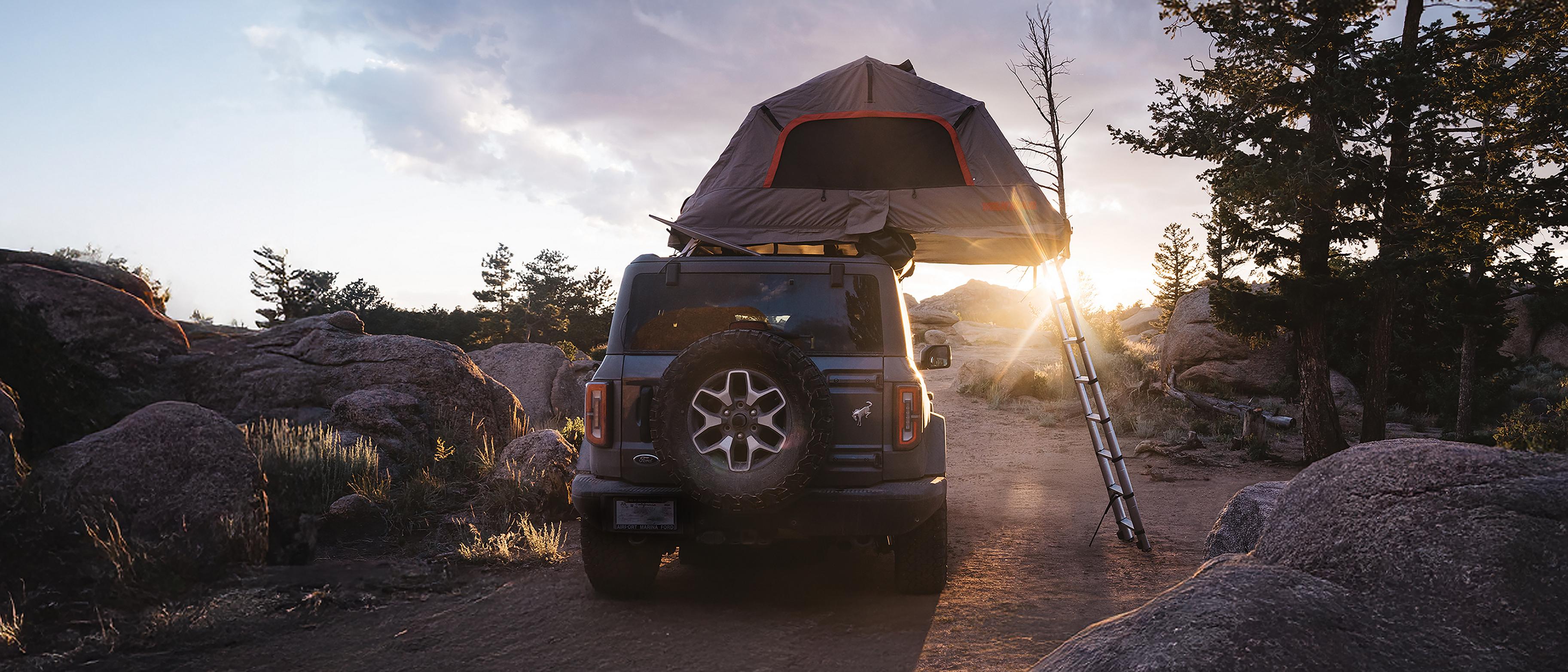 A 2026 Ford Bronco® SUV with an available accessory tent installed and open, parked on a trail at sunset