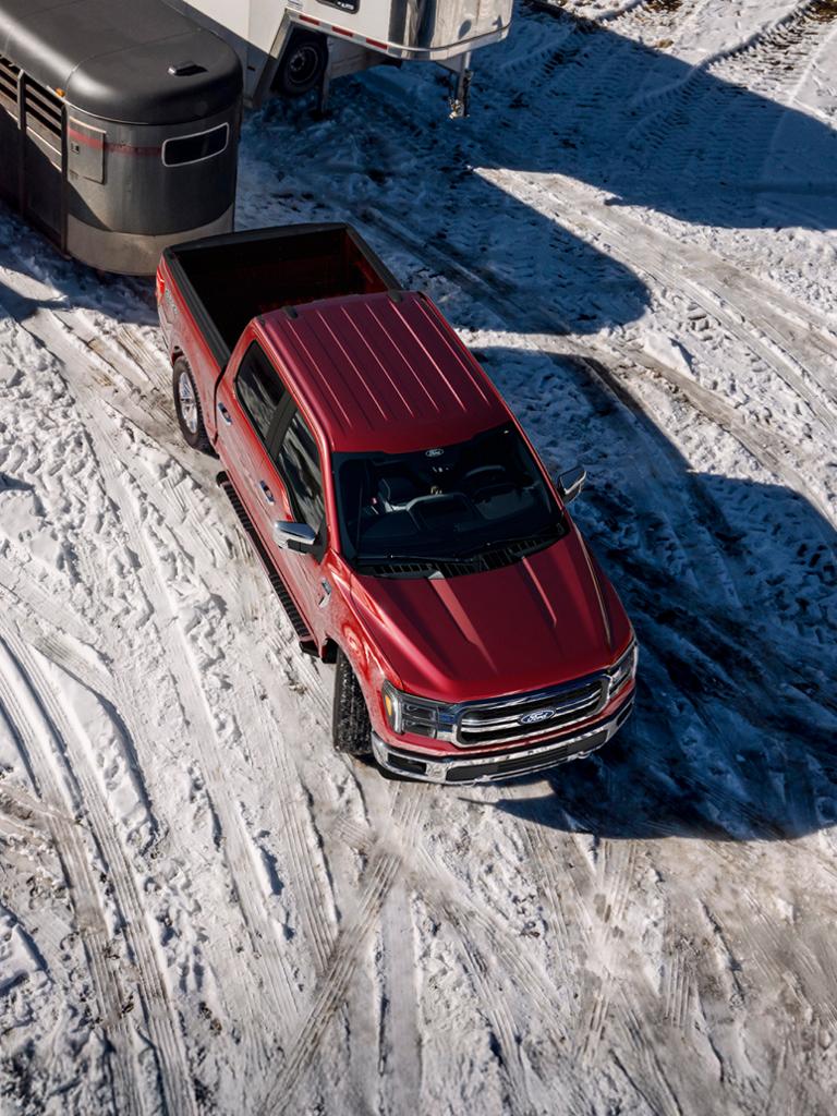 2026 Ford F-150® Lariat® model in Ruby Red Metallic Tinted Clearcoat pulling a horse trailer in the snow