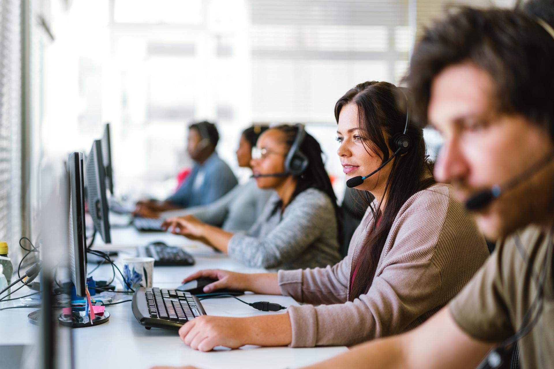 A team of customer service agents, all wearing headsets, seated at a row of computers