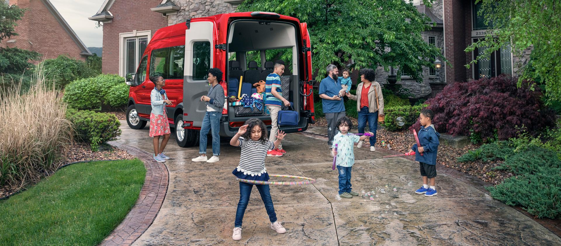 Family gathered around a red 2027 Ford Transit® Passenger van with open doors on a driveway