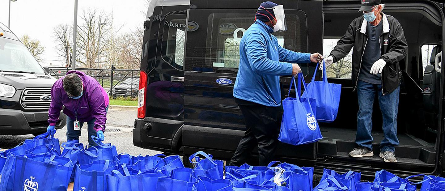 People putting blue bags into a Ford Transit van