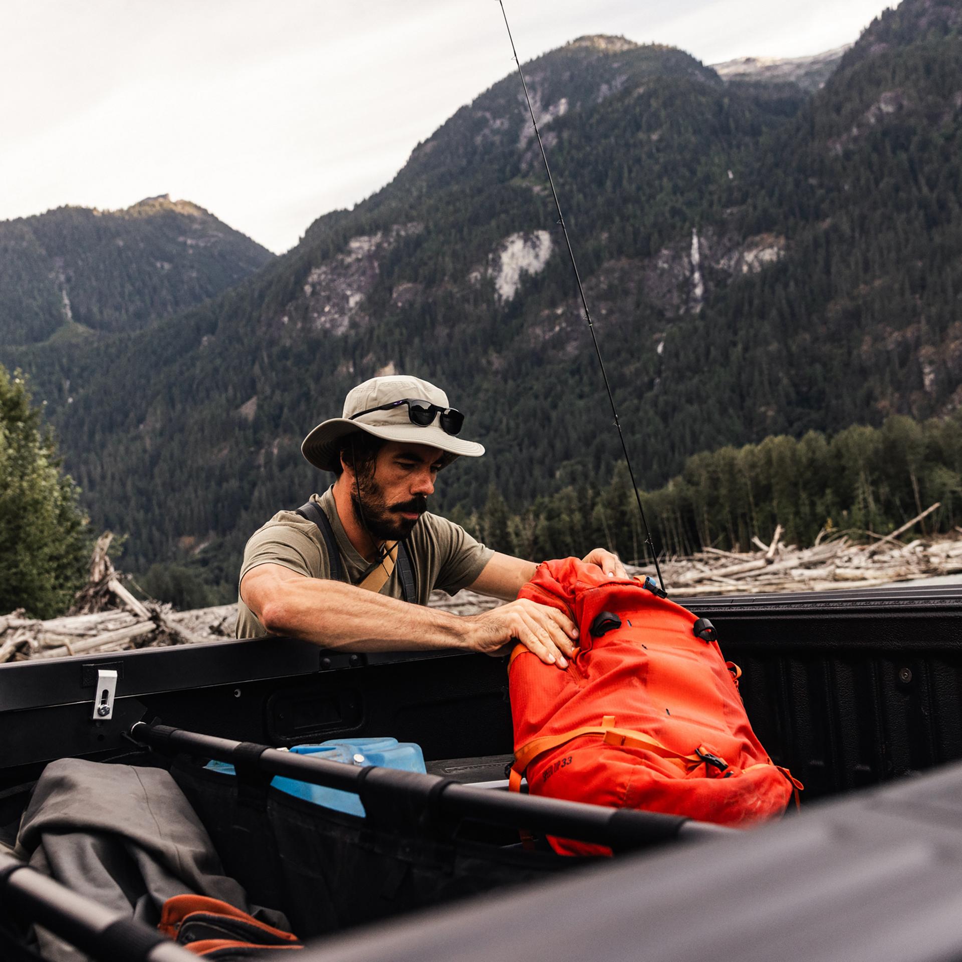 A person in fishing gear grabbing an orange backpack out of the bed of their 2026 Ford Ranger® truck