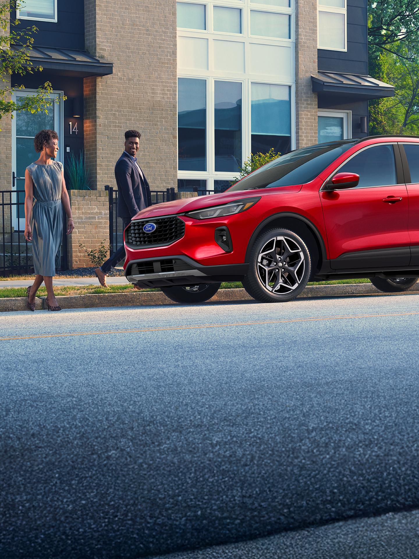 A couple approaches a Ford Escape parked on a city street.