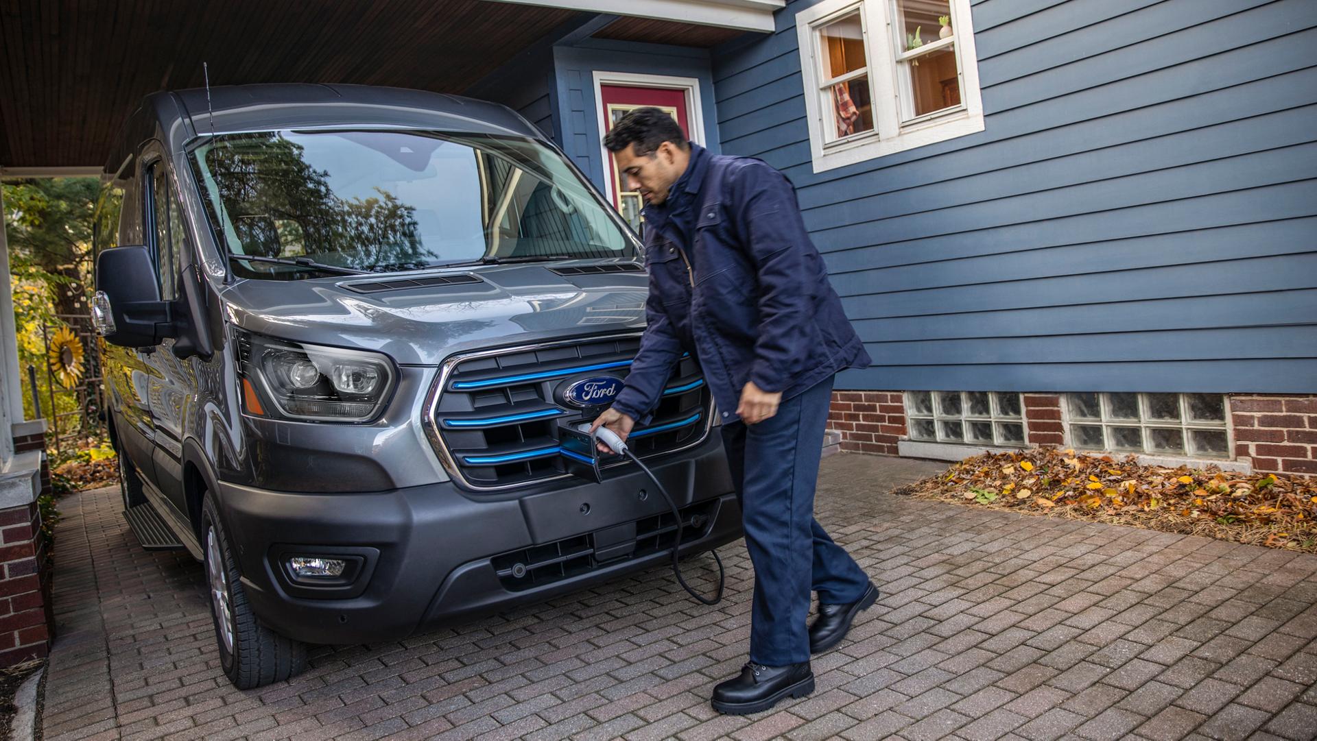 A grey 2025 Ford E-Transit™ parked in a driveway being plugged in to charge