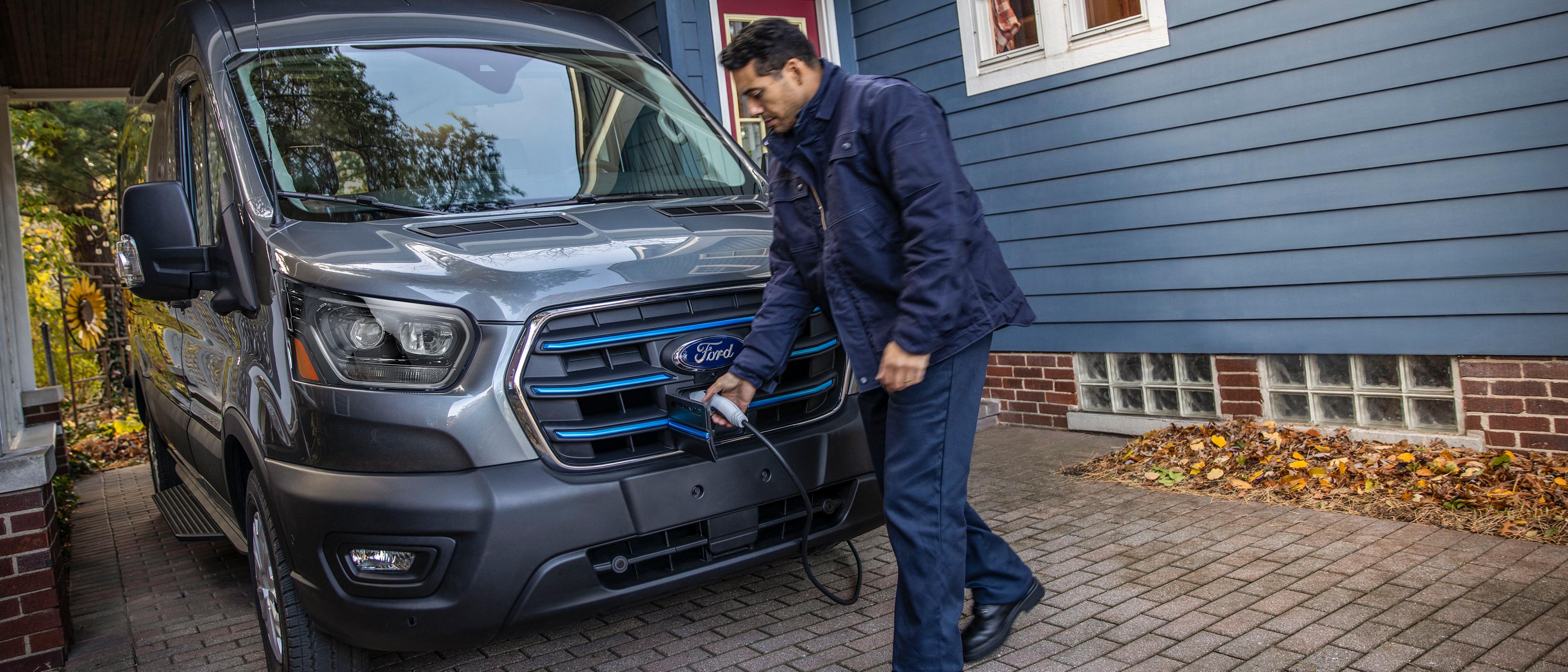A grey 2025 Ford E-Transit™ van parked in a home driveway being charged for the night
