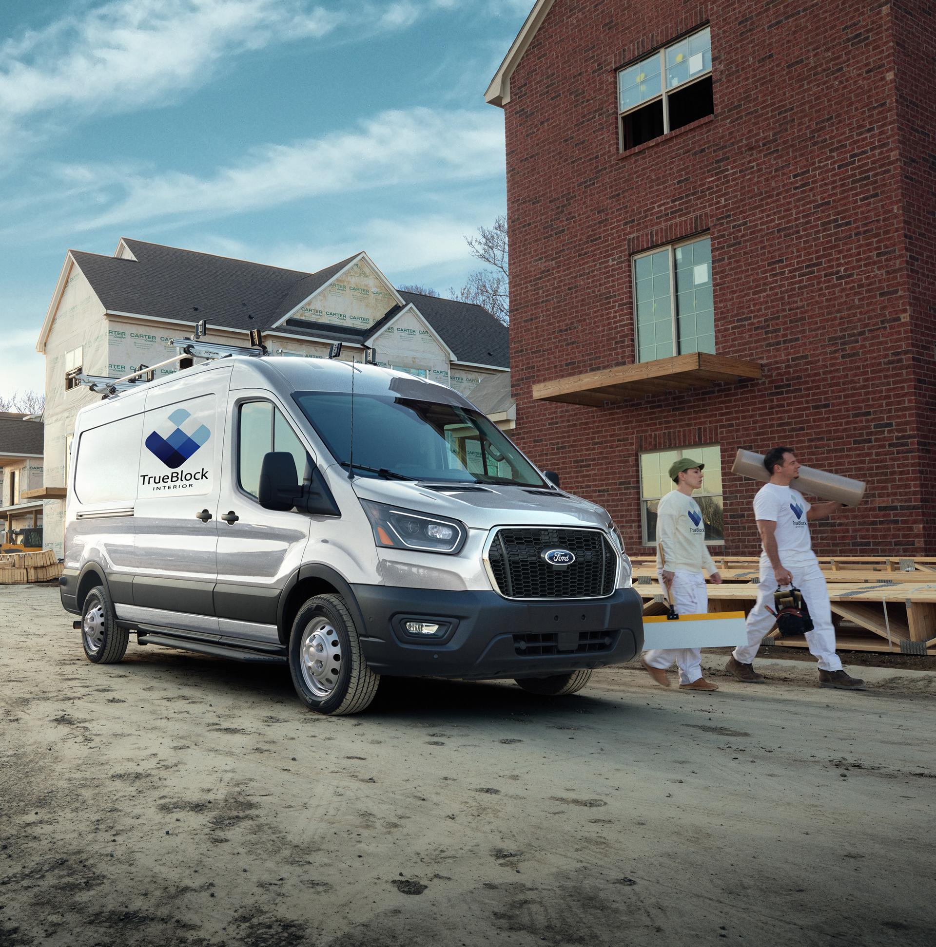 A white 2027 Ford Transit® Van with ladder rack at a construction site with two workers carrying materials