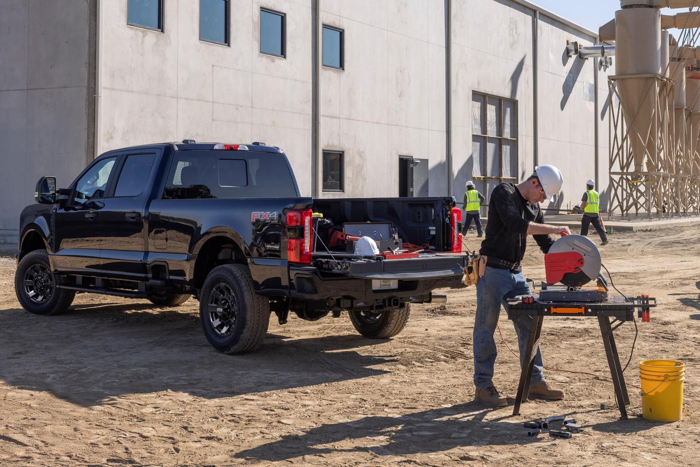 Three-quarter rear of a black Ford Super Duty with its tailgate open. A nearby construction worker is using a circular saw powered the Super Duty’s Pro Power Onboard mobile generator.