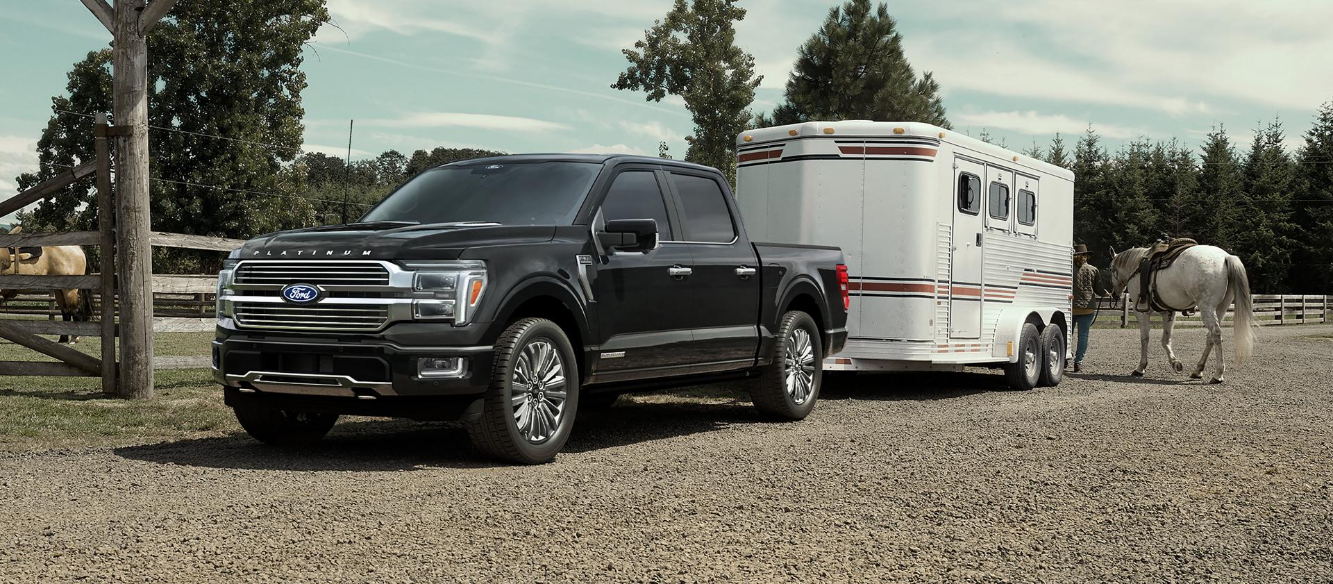 2026 Ford F-150® Platinum® model in Agate Black hitched to a horse trailer parked near a ranch