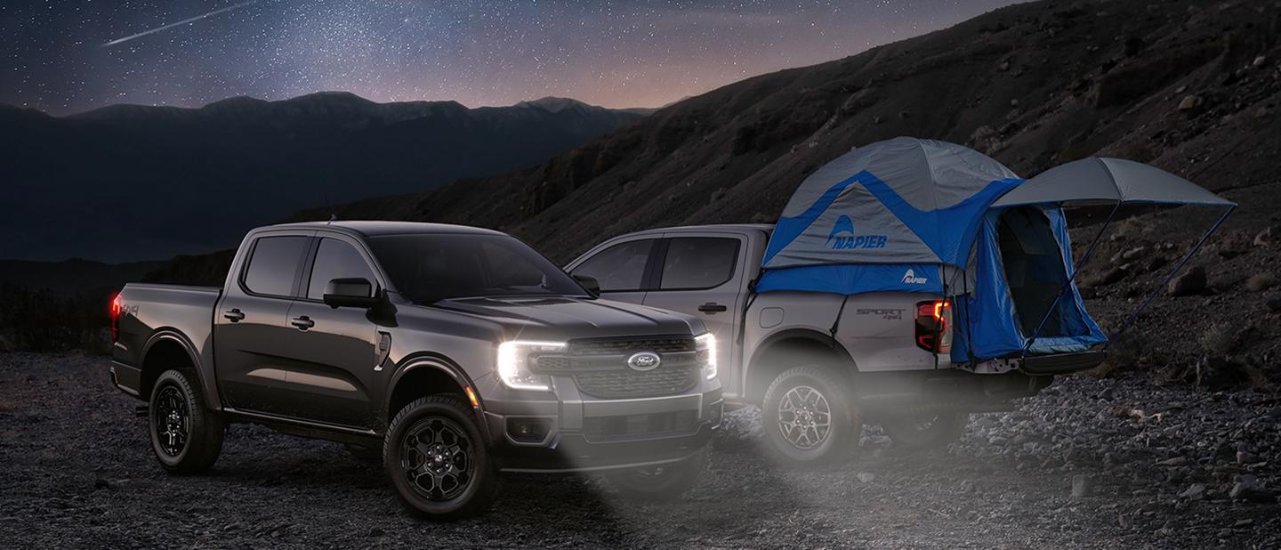 Two 2026 Ford Ranger® trucks parked under a twinkling starry, nighttime sky. One of them with a tent in the truck bed