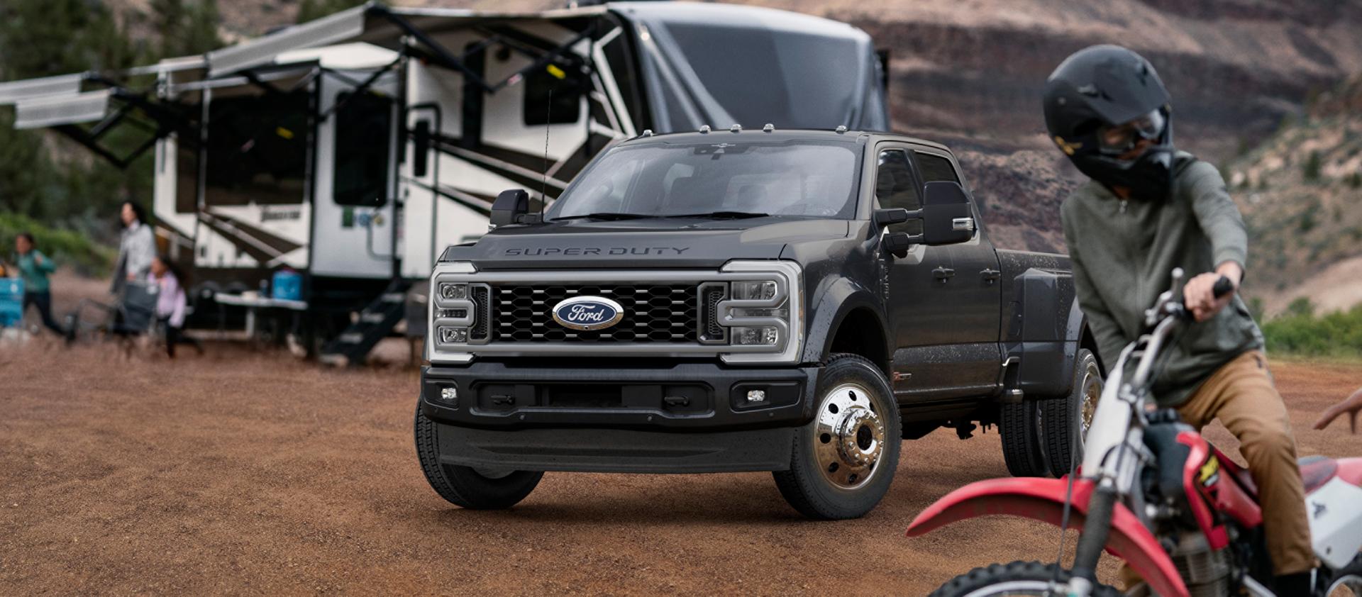 2027 Ford Super Duty® F-450® Platinum® model in Carbonized Grey parked on a campground with a camper in the background