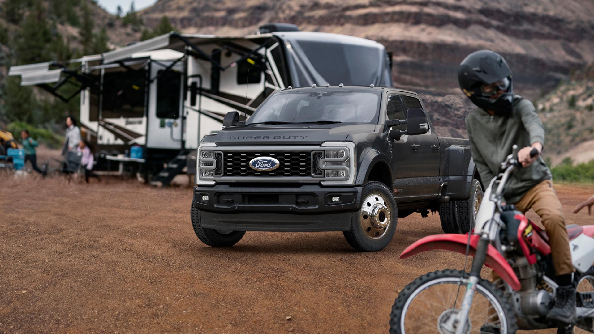 2027 Ford Super Duty® F-450® Platinum® model in Carbonized Grey parked on a campground with a camper in the background