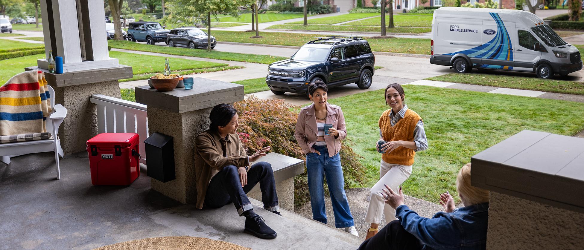 A Ford Mobile service technician greets a Ford owner and their friends on a front porch.
