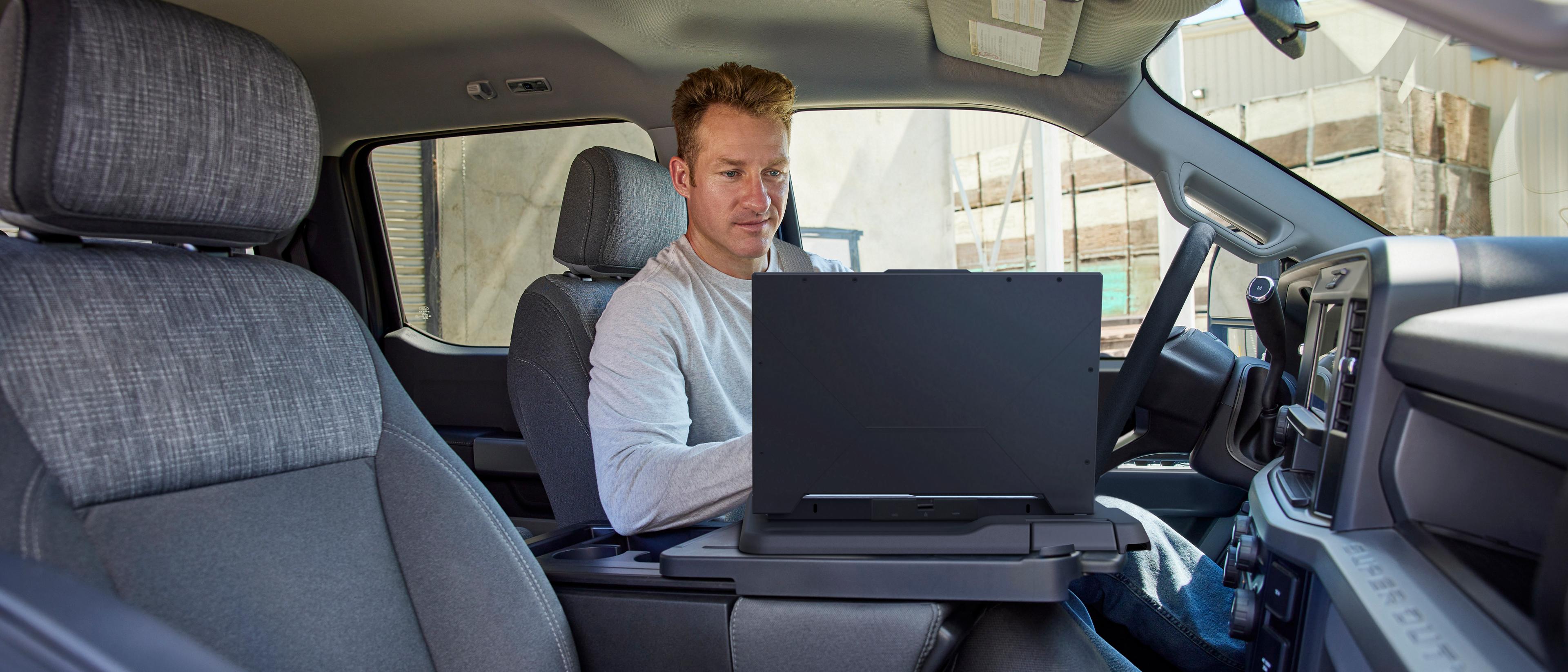 Person working on a laptop using the interior work surface feature inside the cabin of their 2026 Ford Super Duty® truck