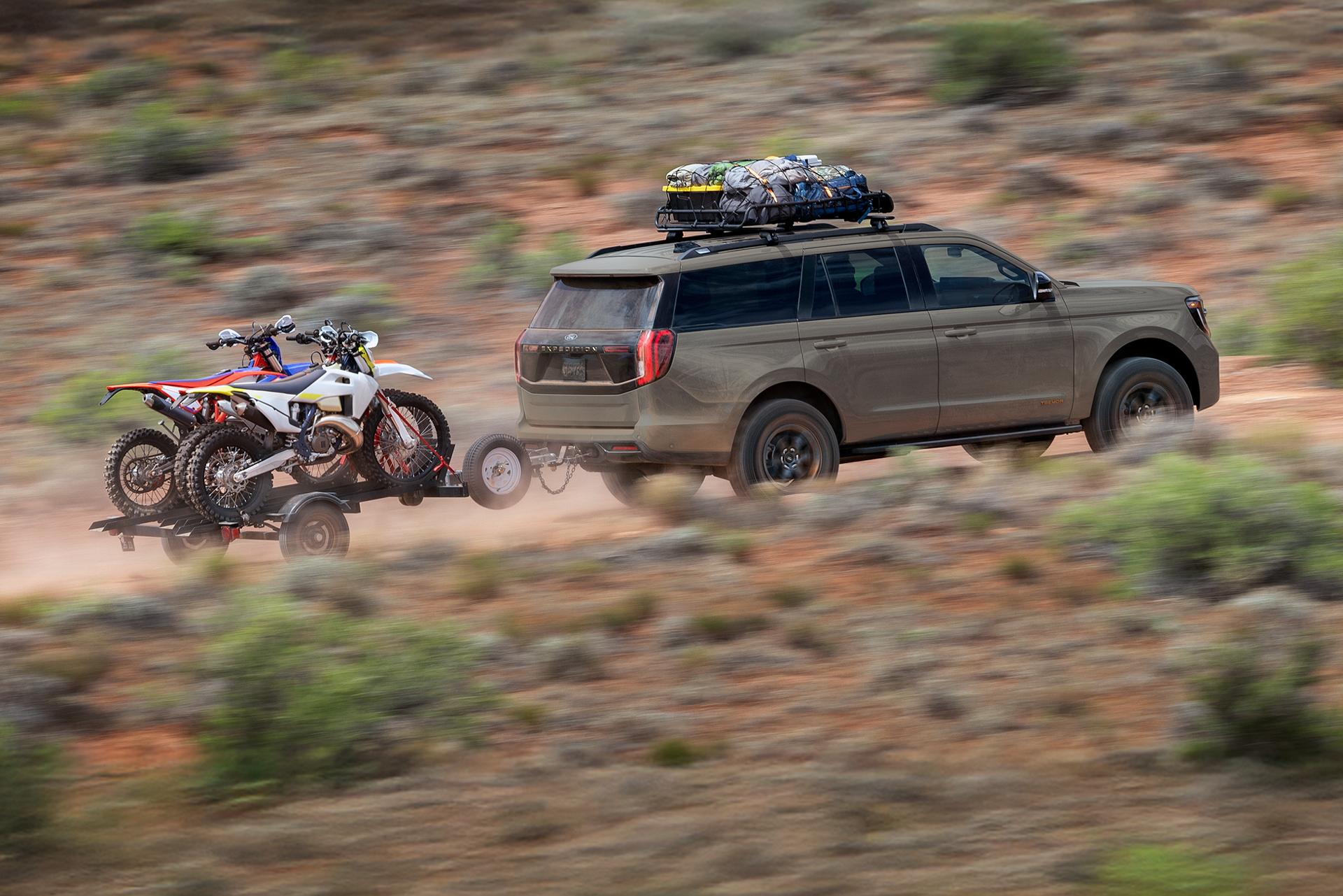 A Ford SUV driving up a rugged hill towing dirtbikes.