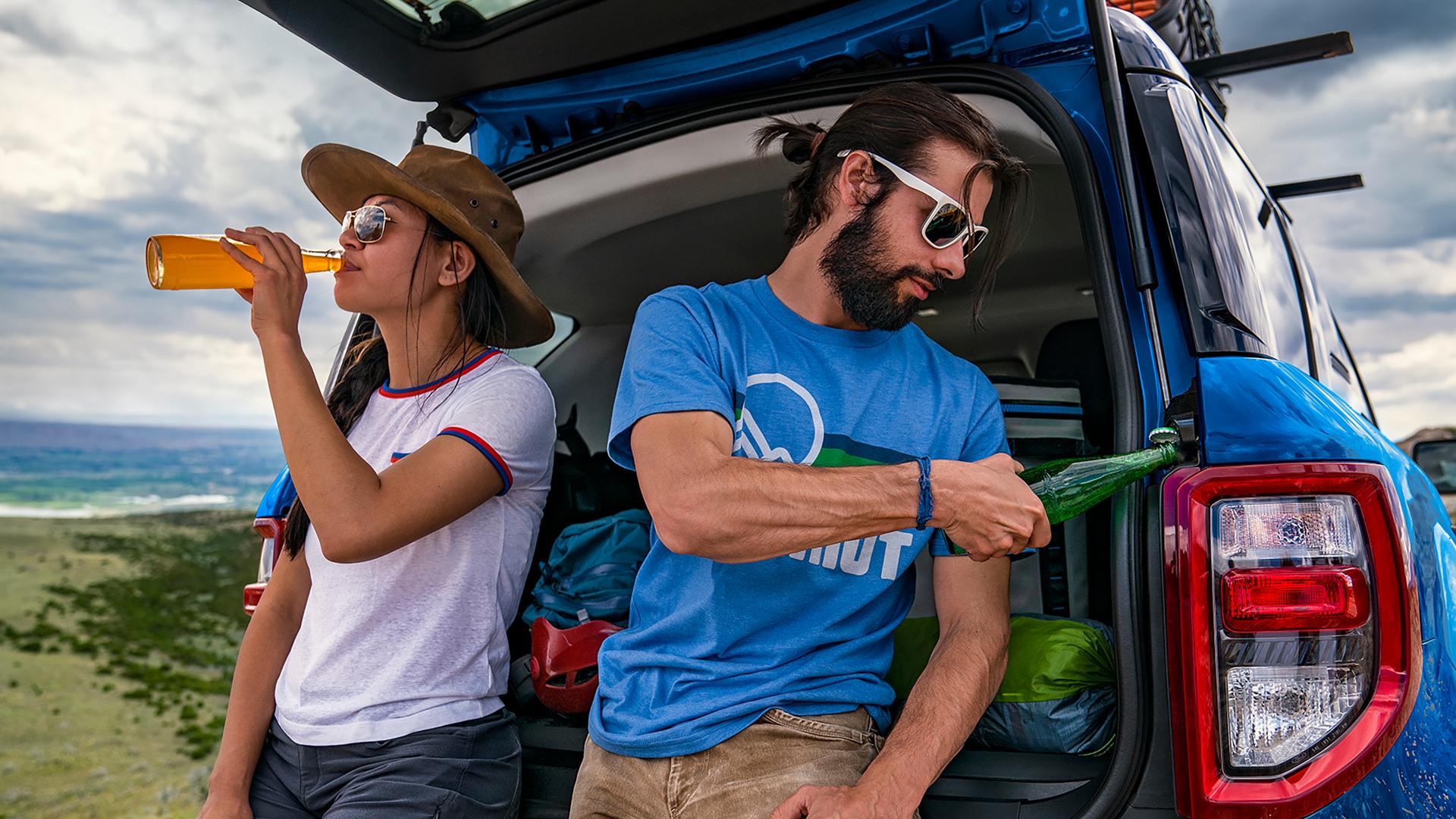 Two people leaning against the tailgate of a 2026 Ford Bronco Sport® SUV and using the built-in bottle opener