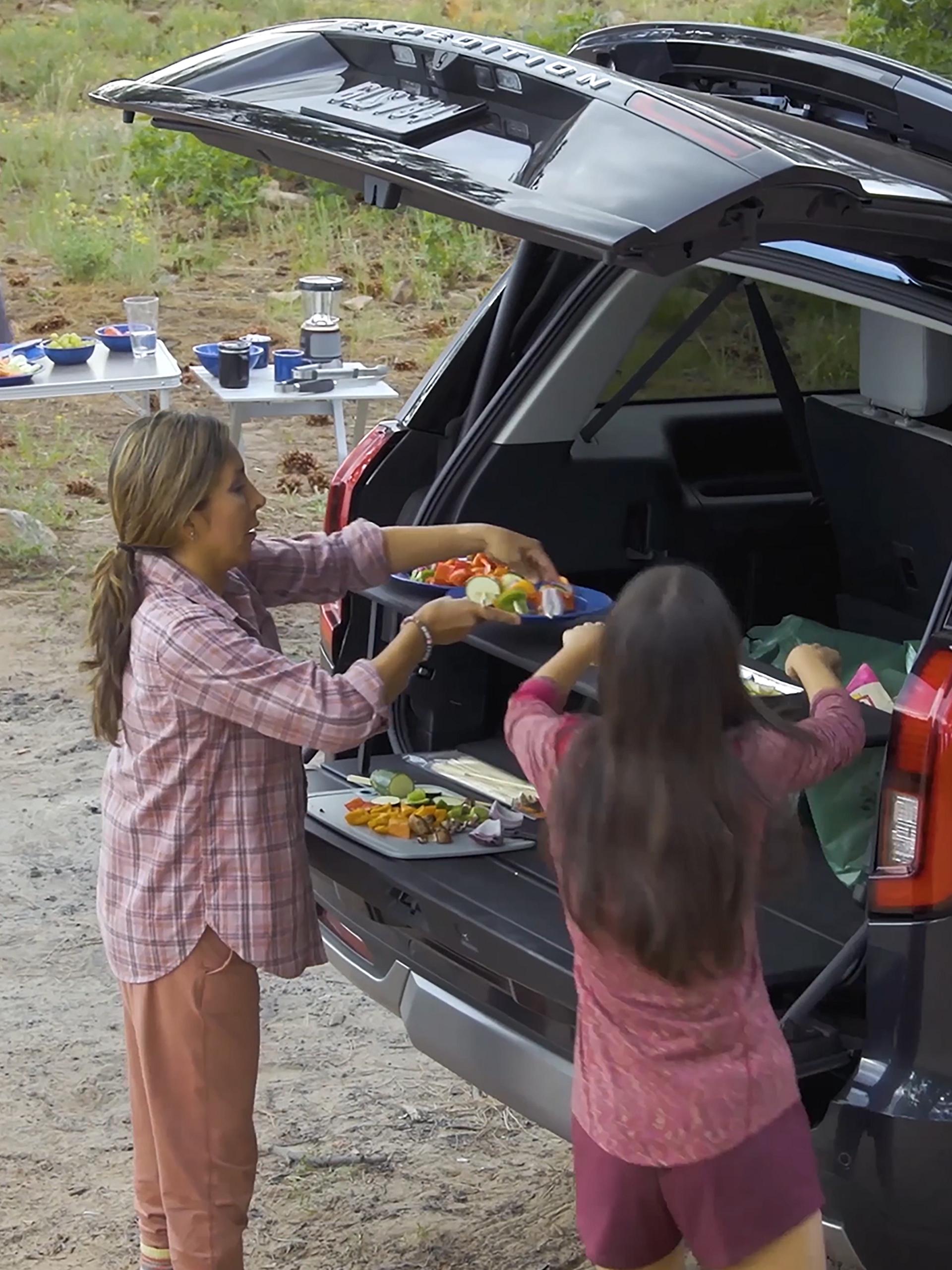 Two people using the available Cargo Tailgate Manager shelf in a parked 2026 Ford Expedition® SUV