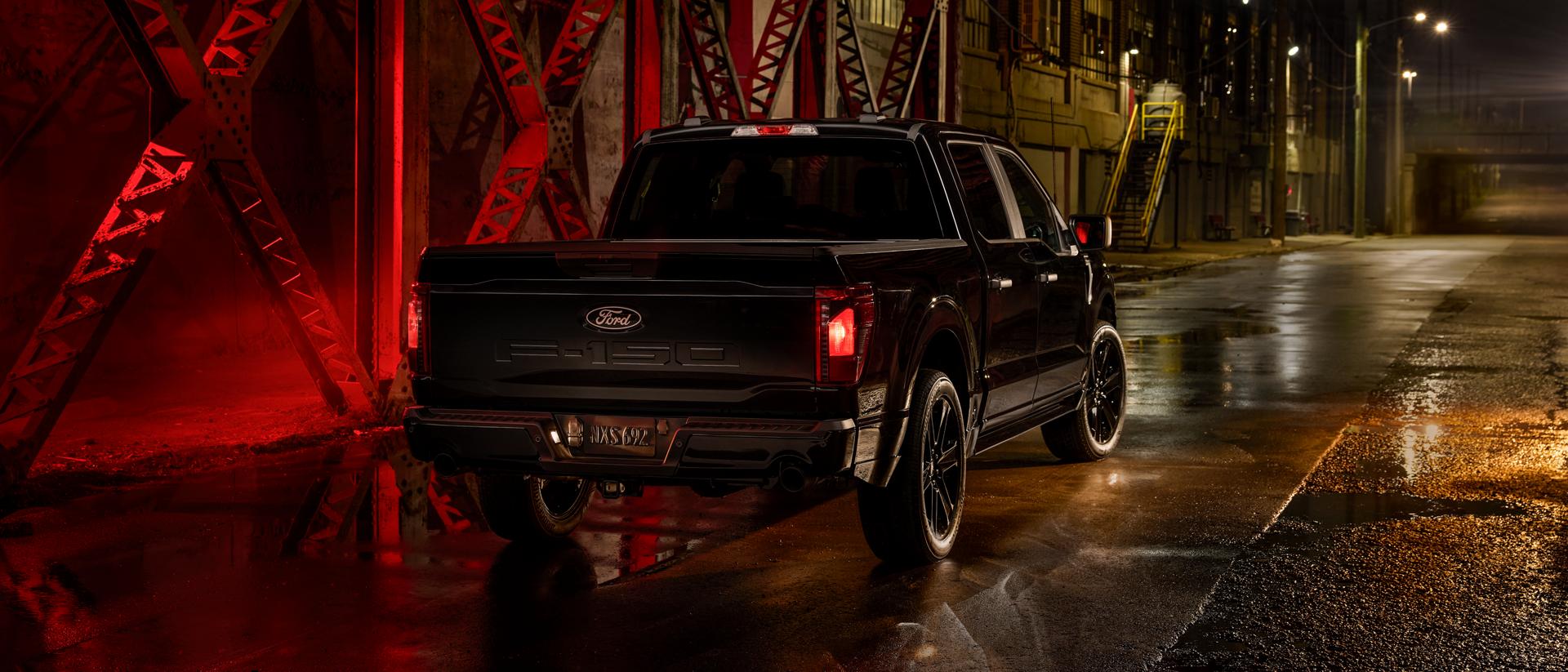 The rear view of a black 2025 F-150® STX with Lobo™ Package truck parked on a vacant city street at night