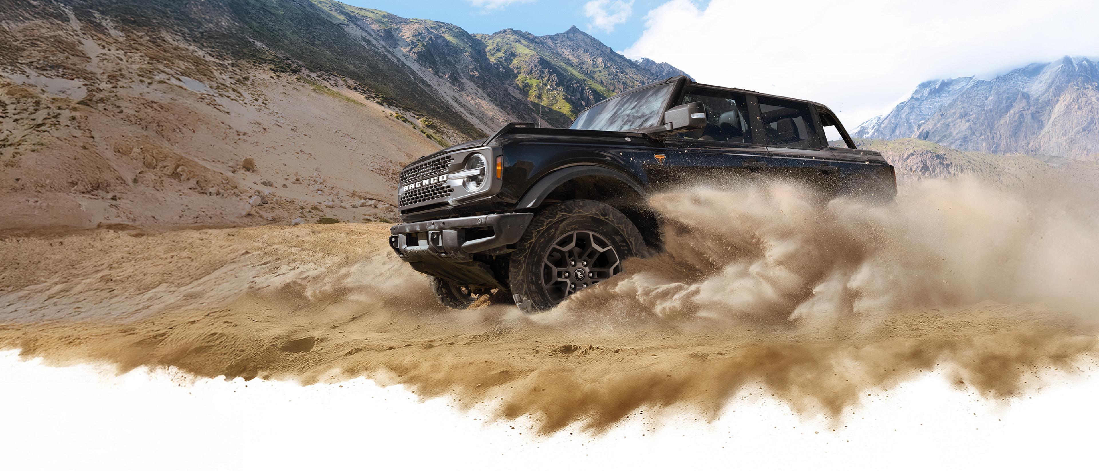 A 2026 Ford Bronco® SUV kicking up dust in a valley beneath rocky hills