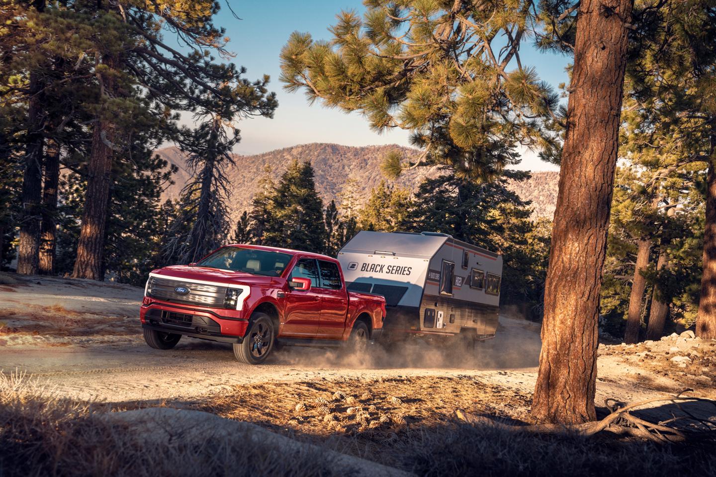 A 2025 Ford F-150® Lightning® is hauling a camper on a dirt road in a scenic location