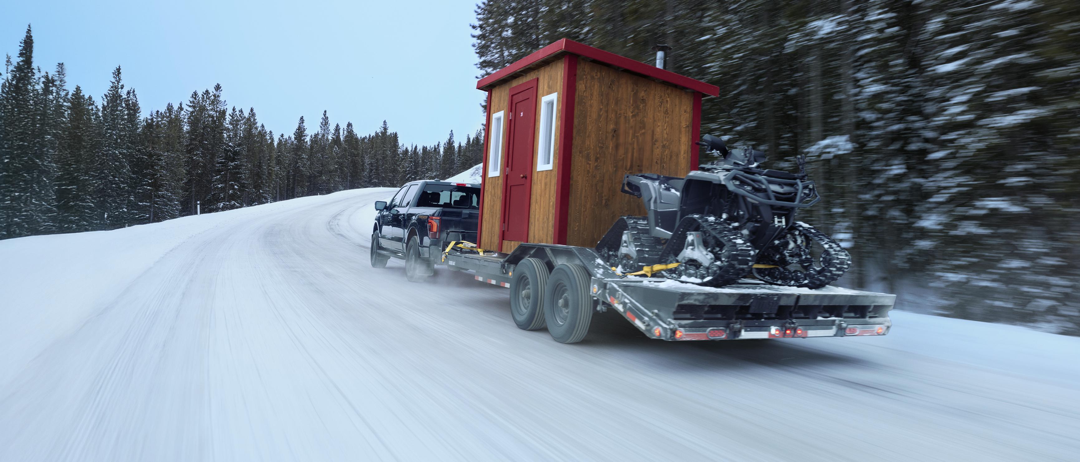 An F-150 Tremor tows an ice fishing hut and an ATV on a trailer through the snow.