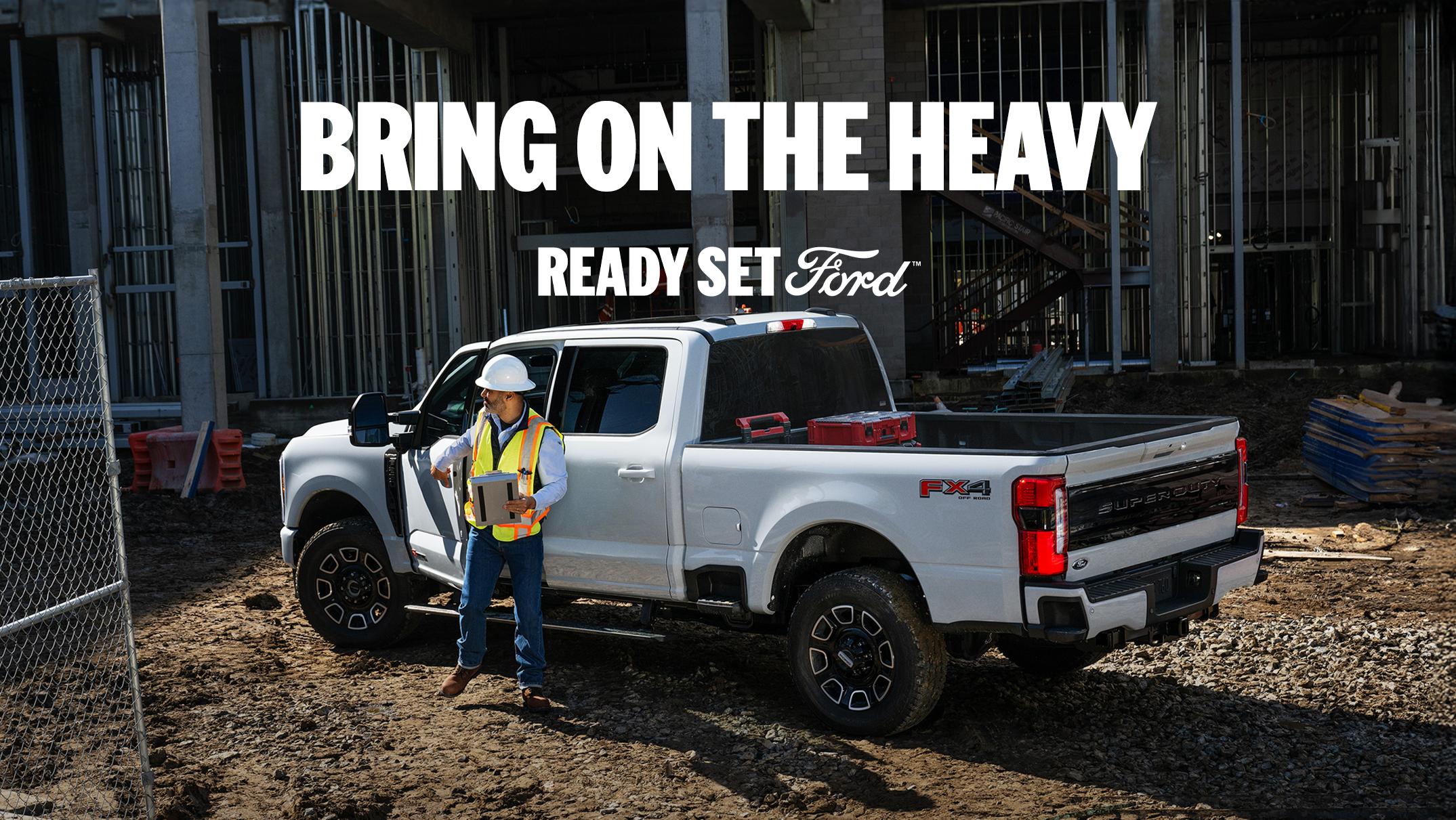 Construction worker stands next to a white Ford Super Duty truck at a construction site