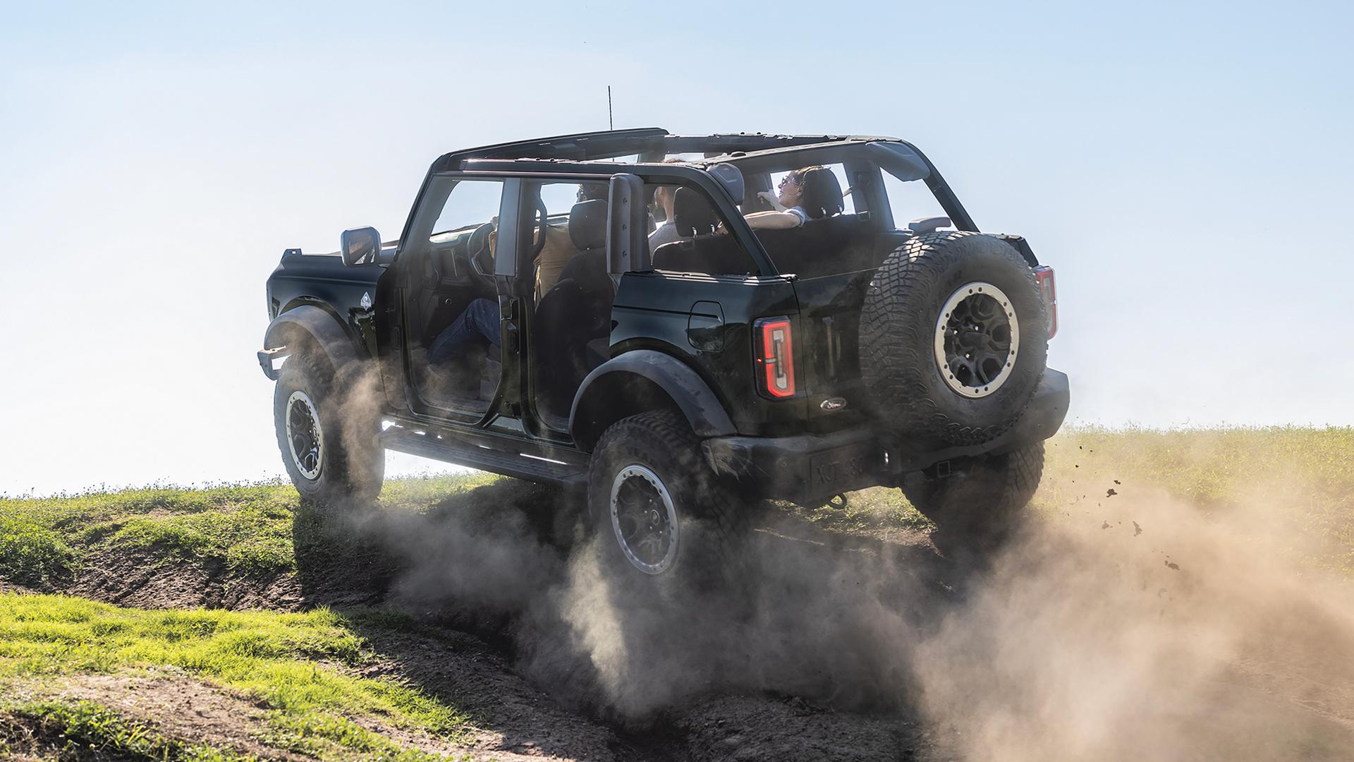 A 2026 Ford Bronco® SUV with the doors removed being driven up a dusty knoll