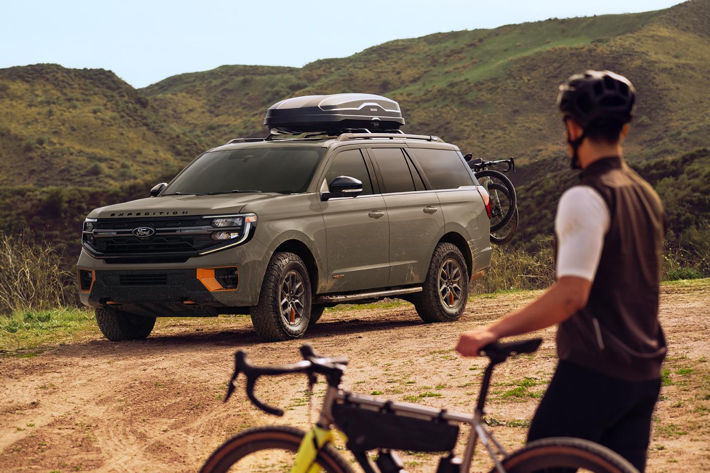 A person with a bicycle standing next to a Ford Expedition® with a roof box accessory