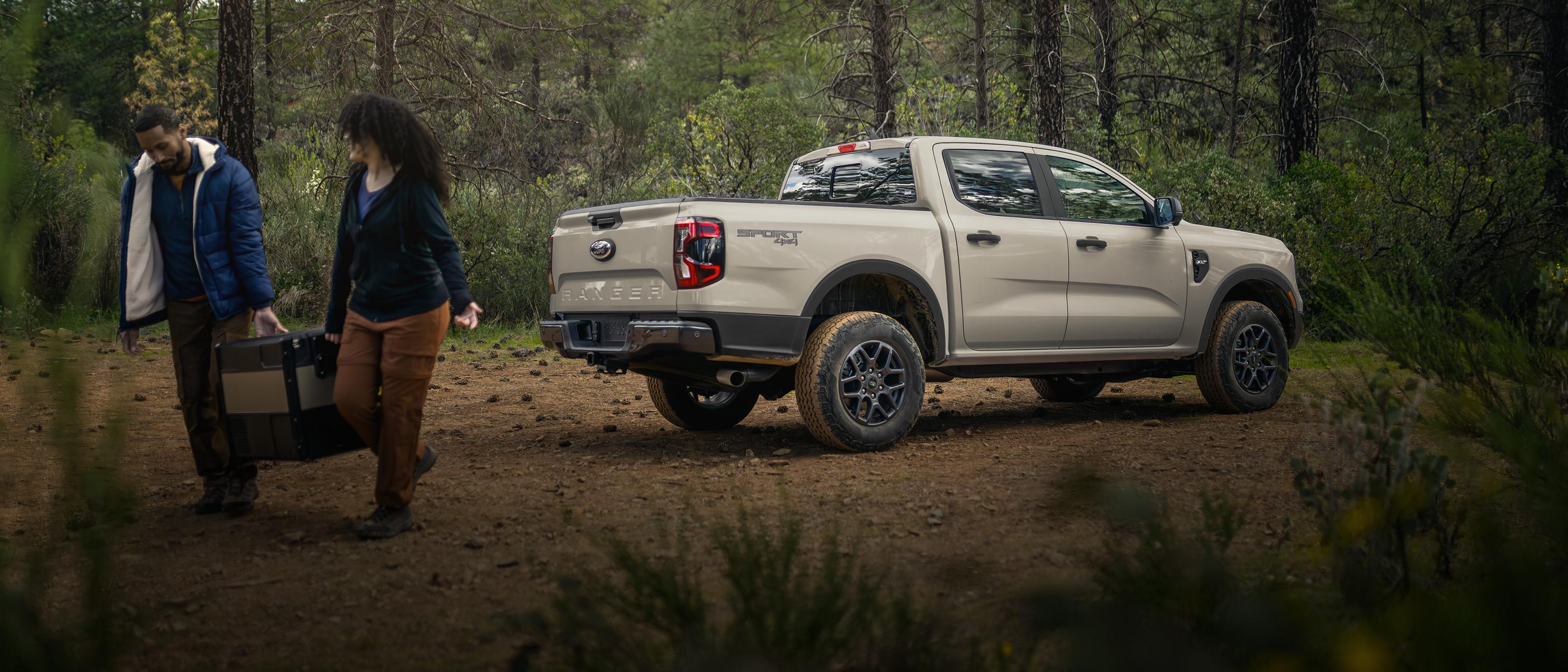 A 2025 Ford Ranger® parked in the woods with a couple walking away from it carrying luggage