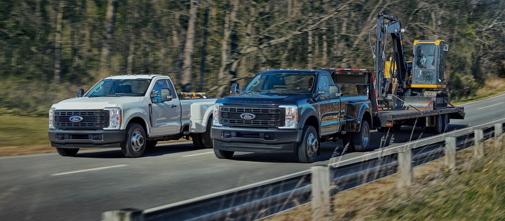 Two 2026 Ford Super Duty® trucks, one with equipment in the bed and the other pulling a large trailer on a paved road