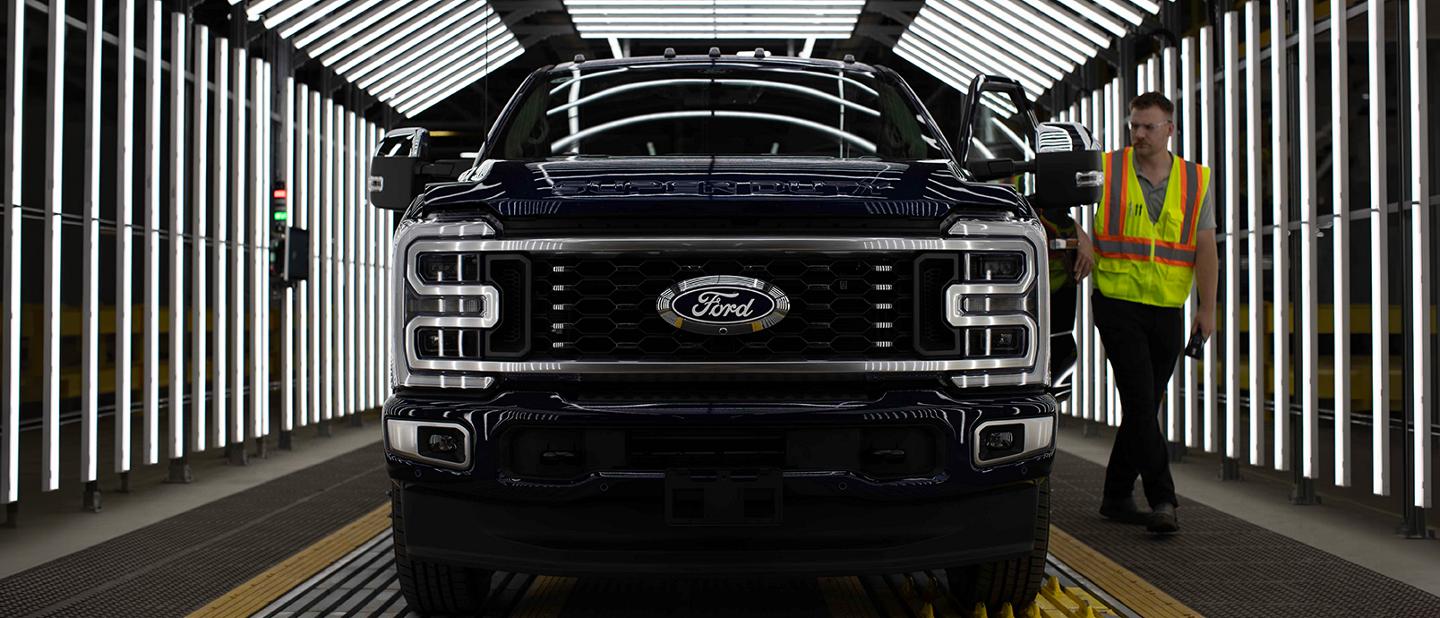 A black Ford Super Duty truck in an inspection tunnel with a man in a safety vest walking alongside it.
