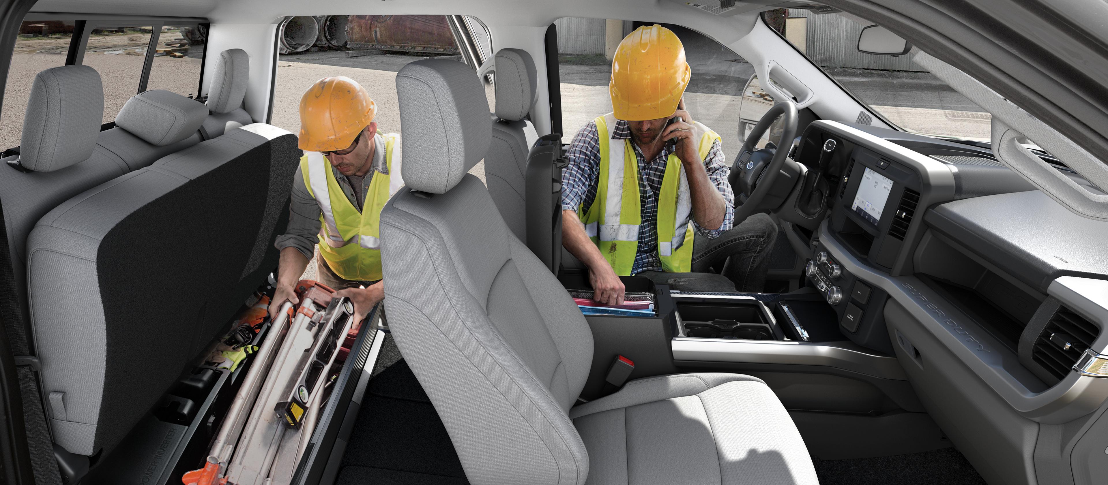 Two workers in hard hats access the storage areas inside the cab of the 2026 Ford Super Duty® Chassis Cab