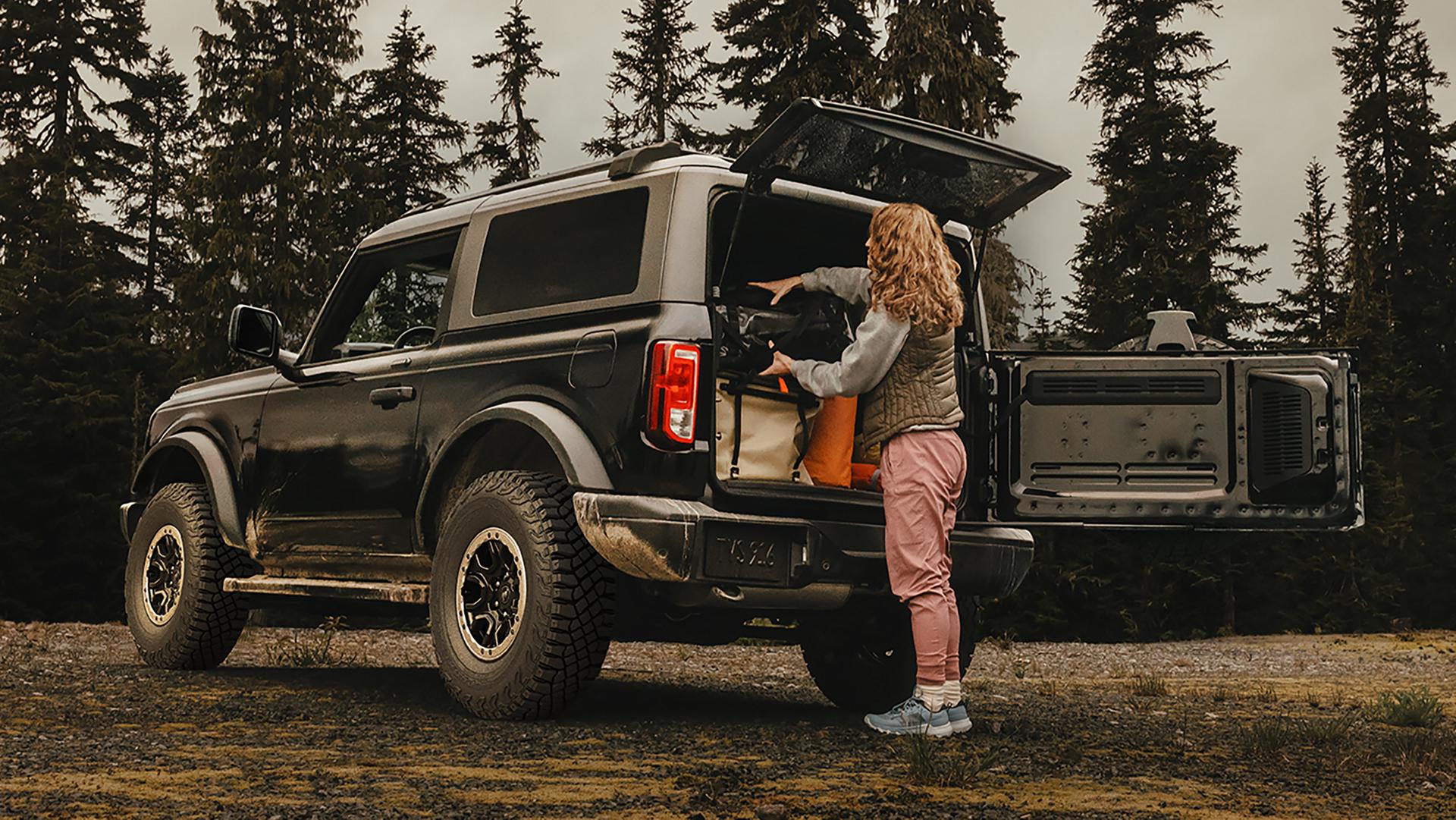 A woman unloading gear from the back of a 2026 Ford Bronco® SUV with the swing gate open