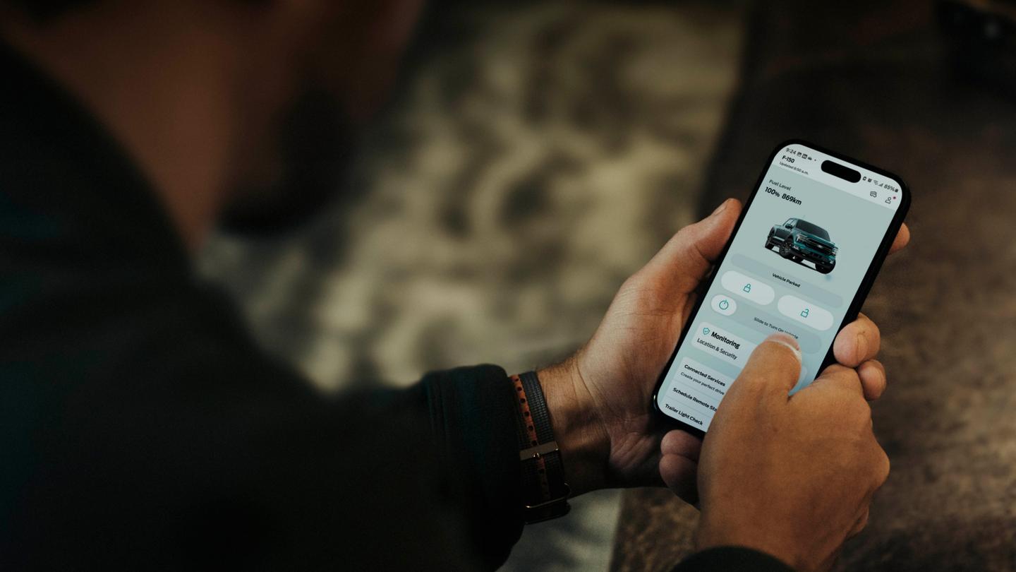 Person holding a smartphone displaying a screen in the Ford app.