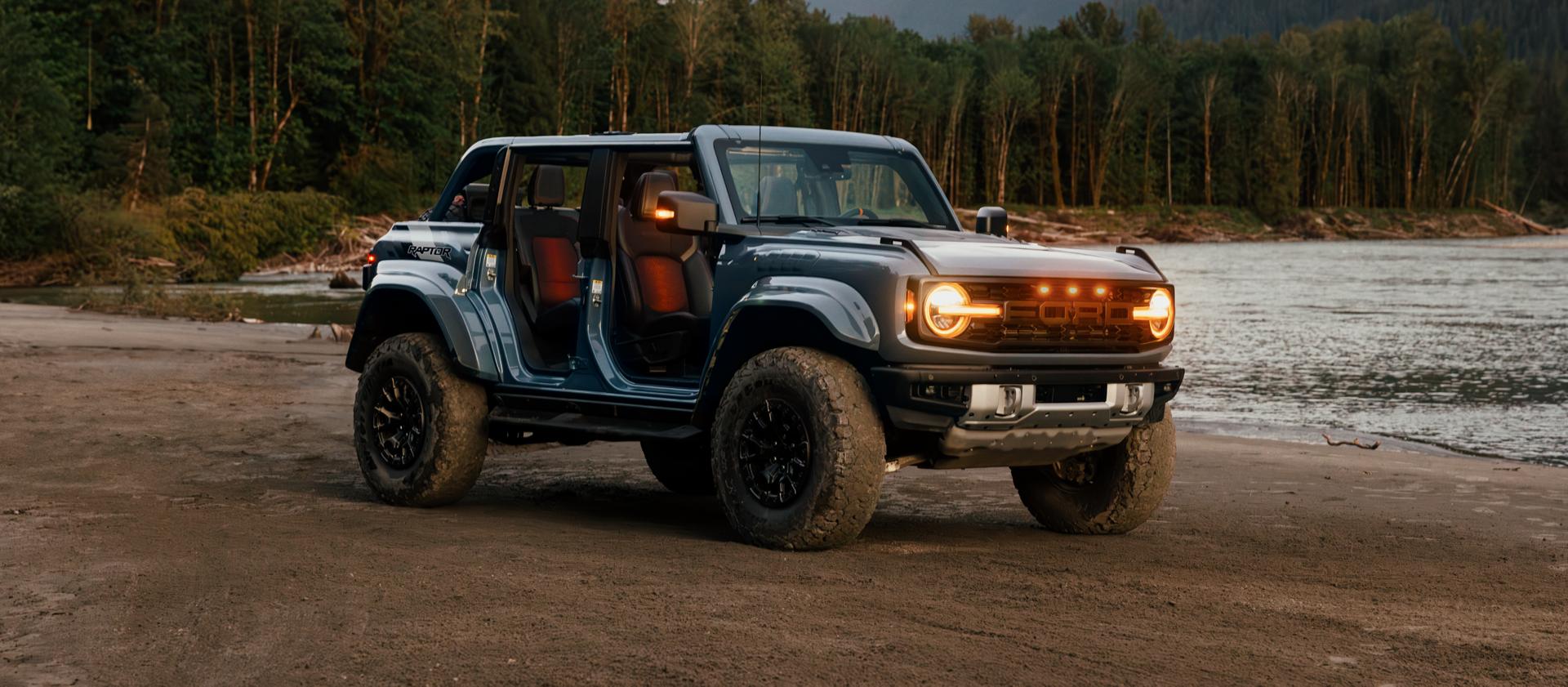 A 2025 Ford Bronco® SUV with the doors off and lights on, parked near a lake in the forest