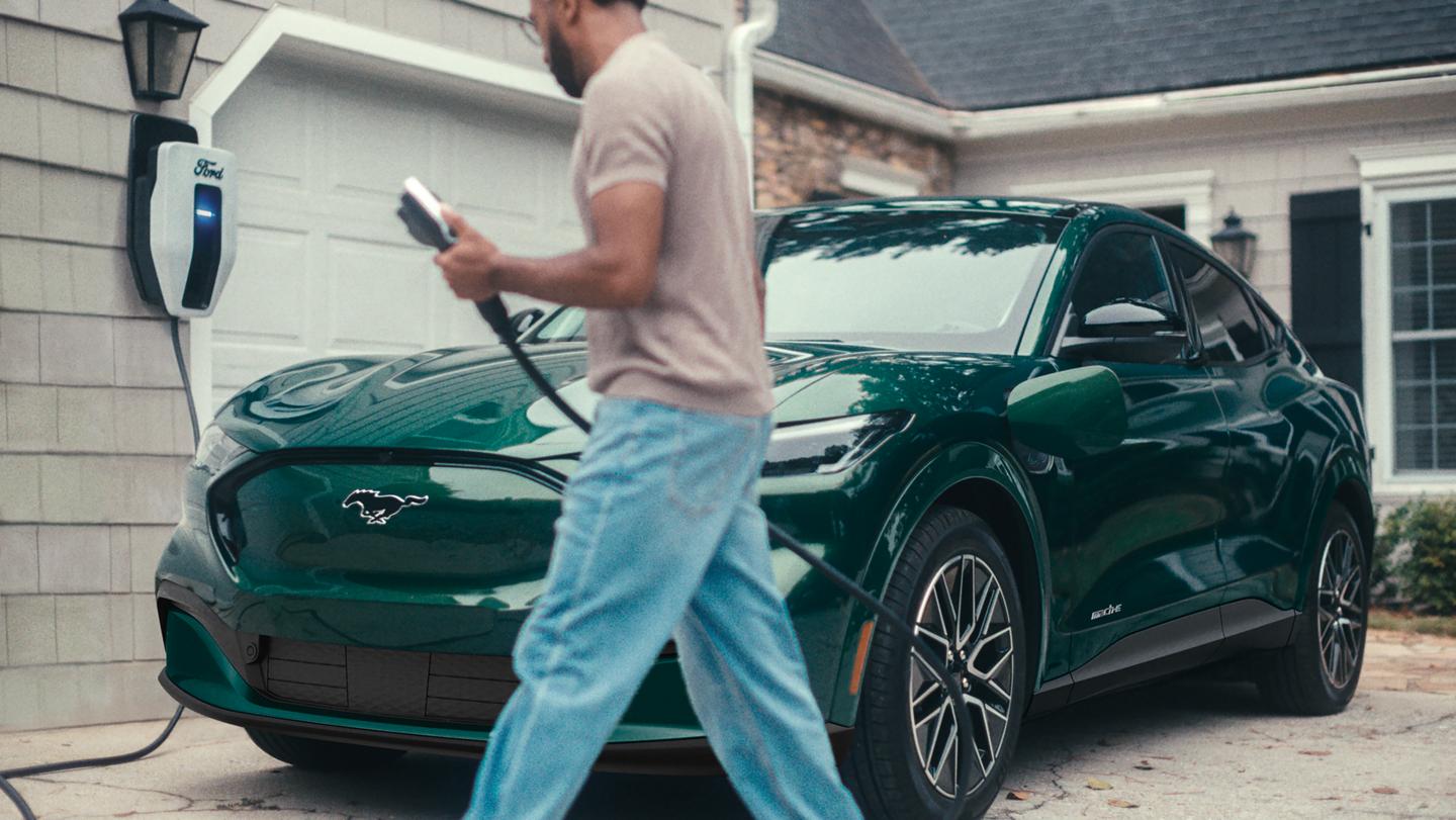 A man holds an EV charging cable near a Ford Mustang Mach-E.