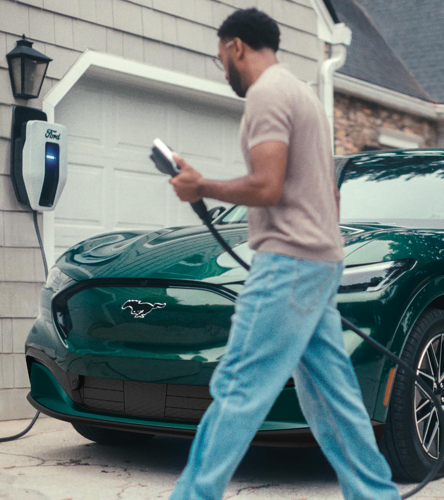 A man holds an EV charging cable near a Ford Mustang Mach-E.