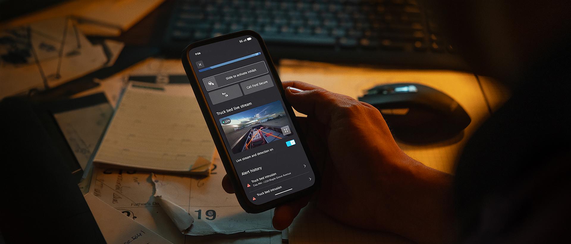 Close-up of a person's hand holding a smartphone and checking on their truck bed via the Ford Truck Bed Camera