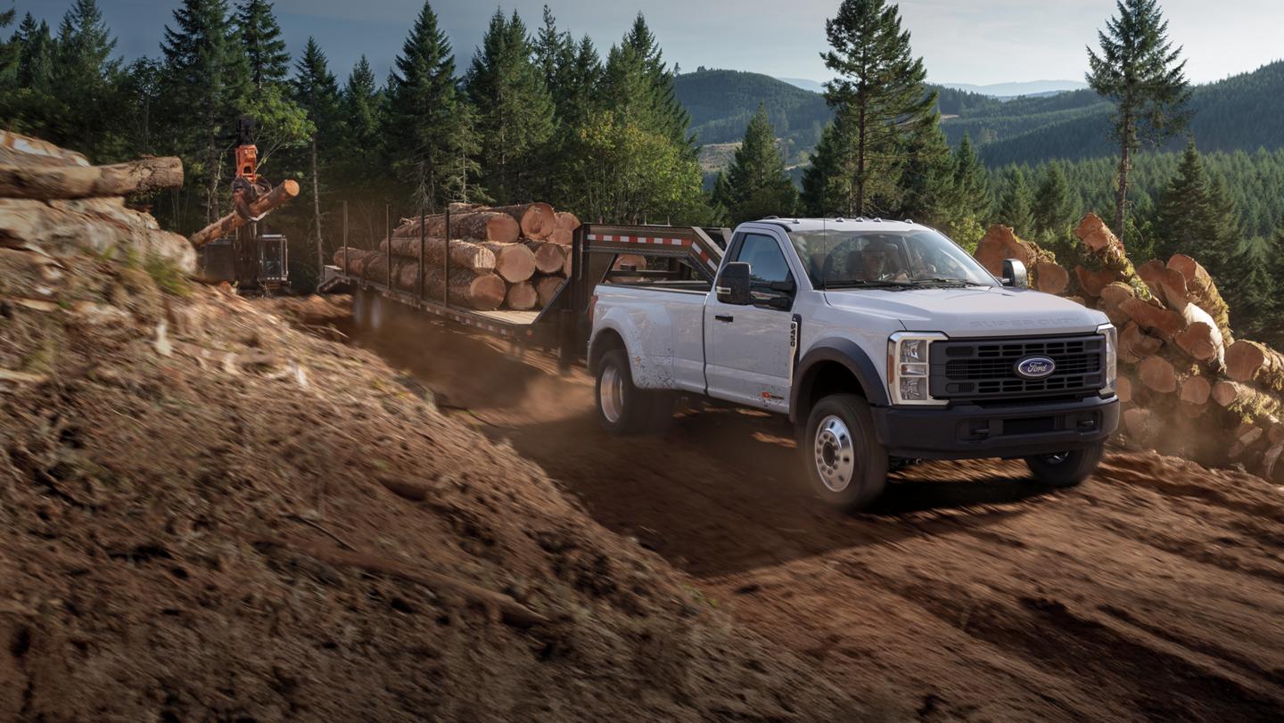 2026 Ford Super Duty® F-450® XL model with the STX® Appearance Package pulling a trailer of tree trunks on a dirt road