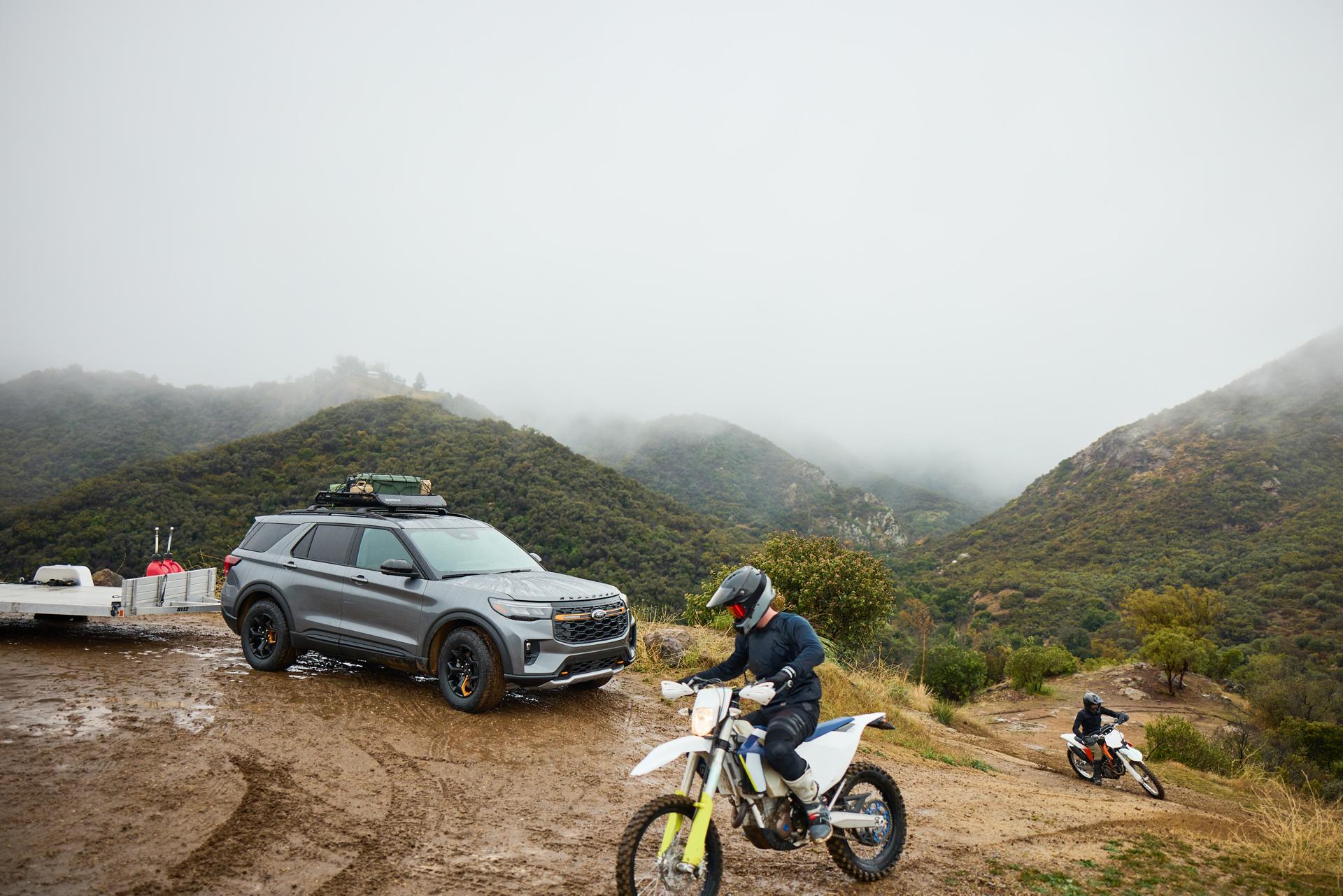 A person rides a dirt bike near a Ford Explorer.
