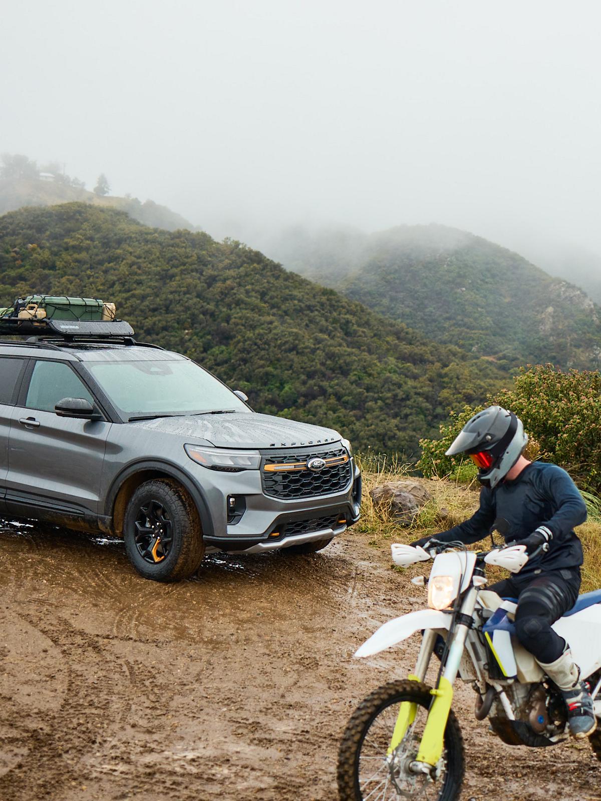 A person rides a dirt bike near a Ford Explorer.