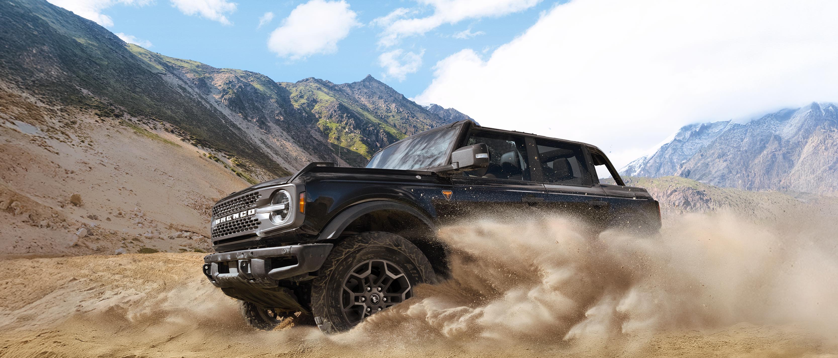 A 2026 Ford Bronco® SUV kicking up dust in a valley beneath rocky hills