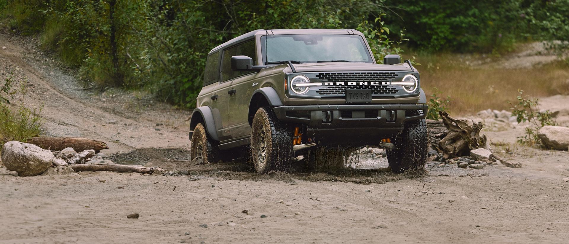 Bronco driving up a muddy mountain trail.