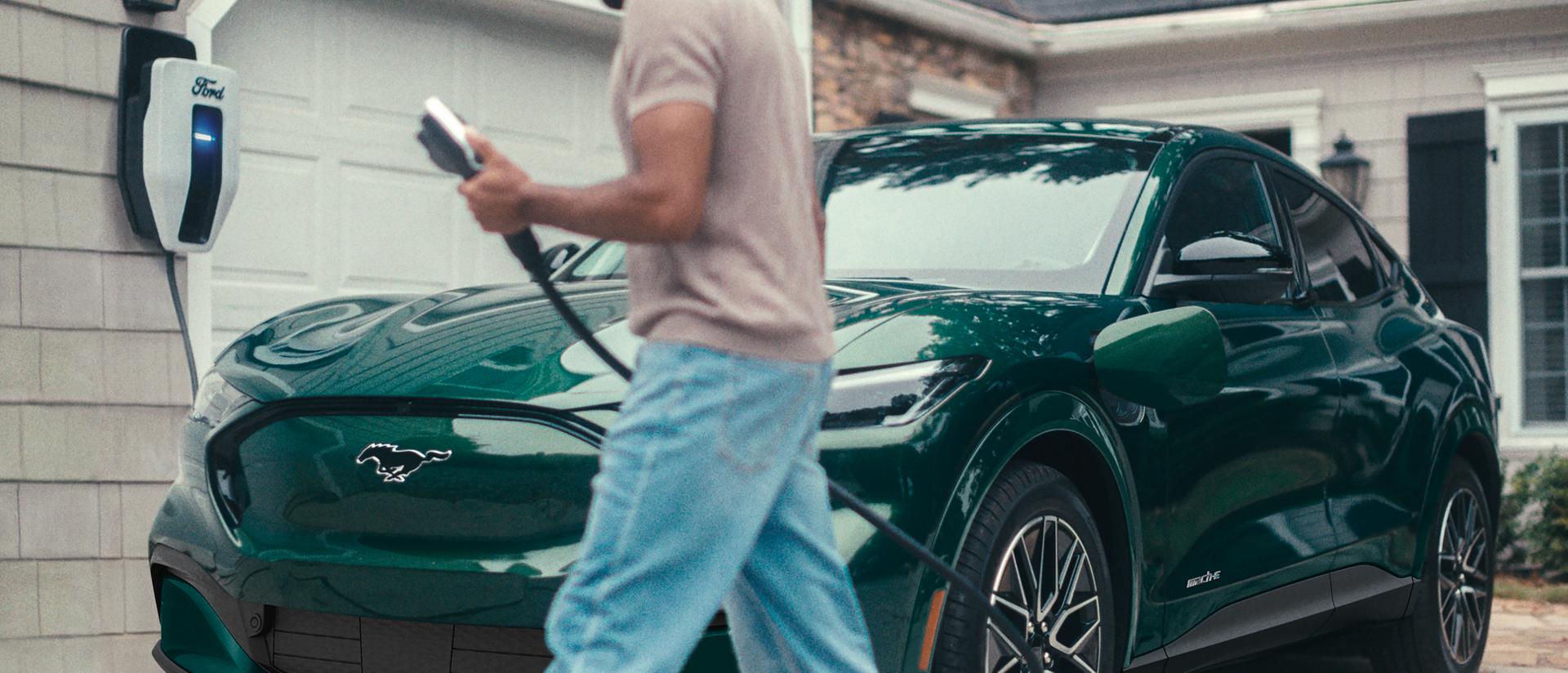 Man plugs in a 2025 Ford Mustang Mach-E® parked outside a home